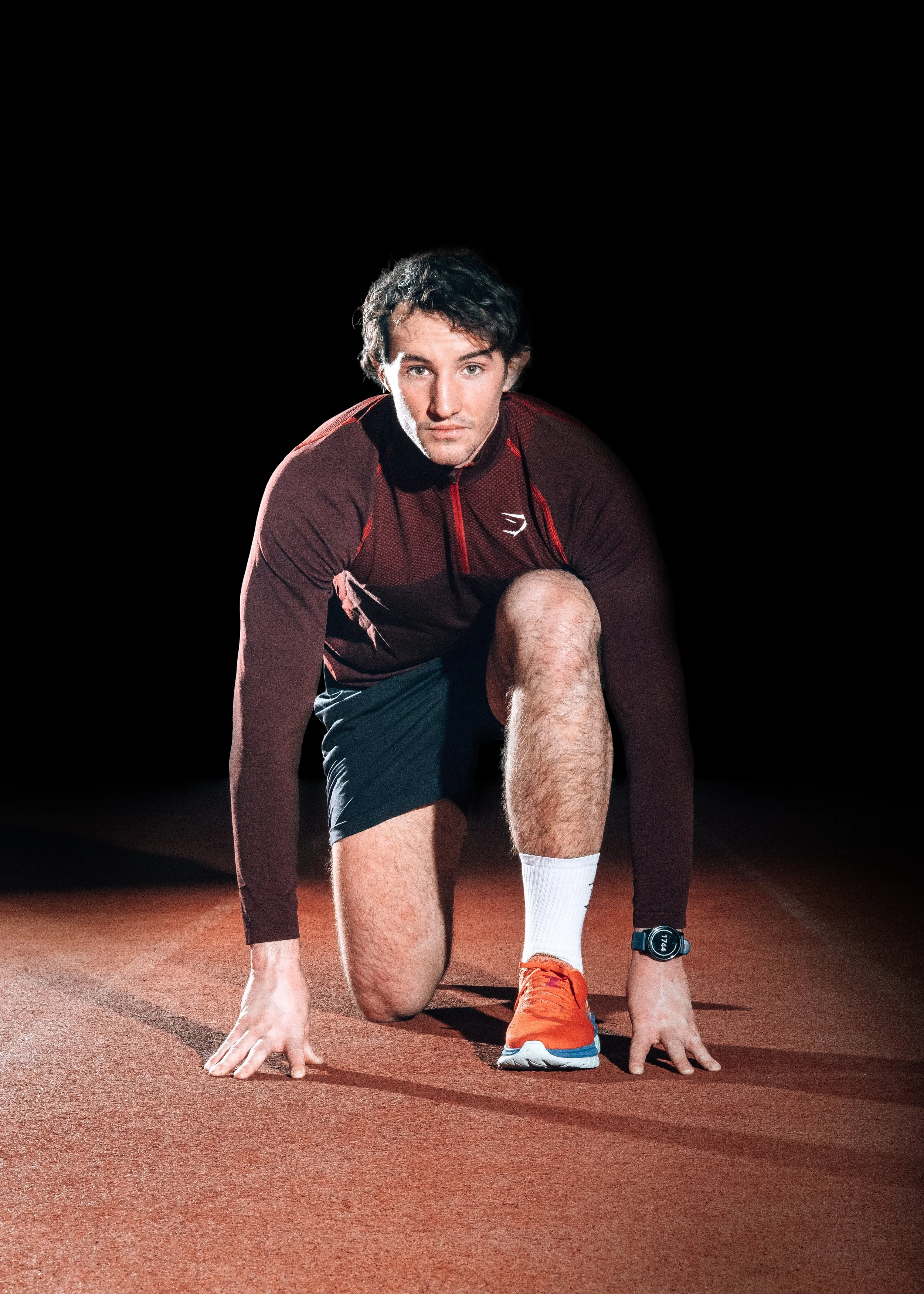 Man i löparkläder i startposition på löparbana, mörk bakgrund.