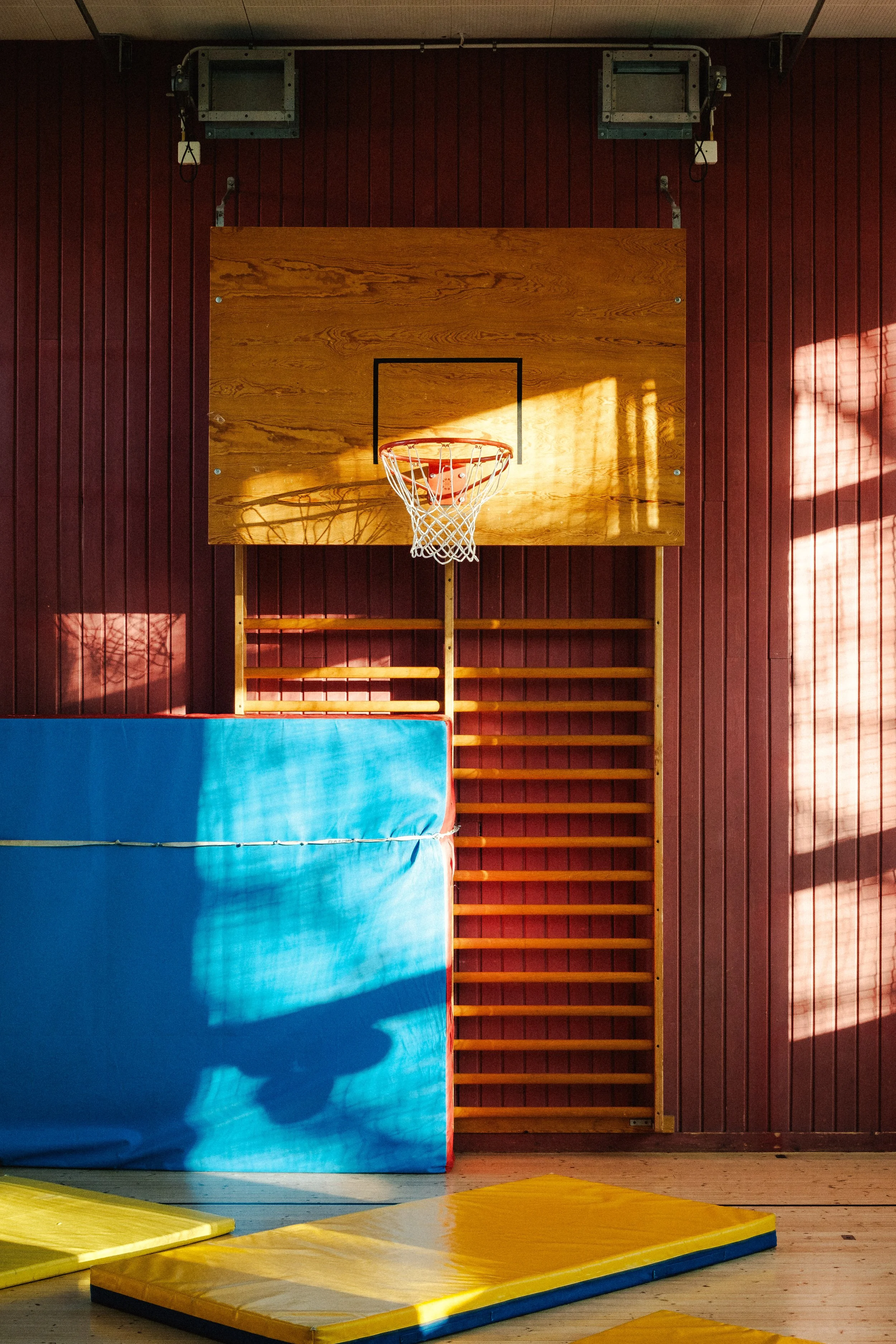 En inomhus basketplan med en basketkorg, madrasser och väggarna är av träpanel.