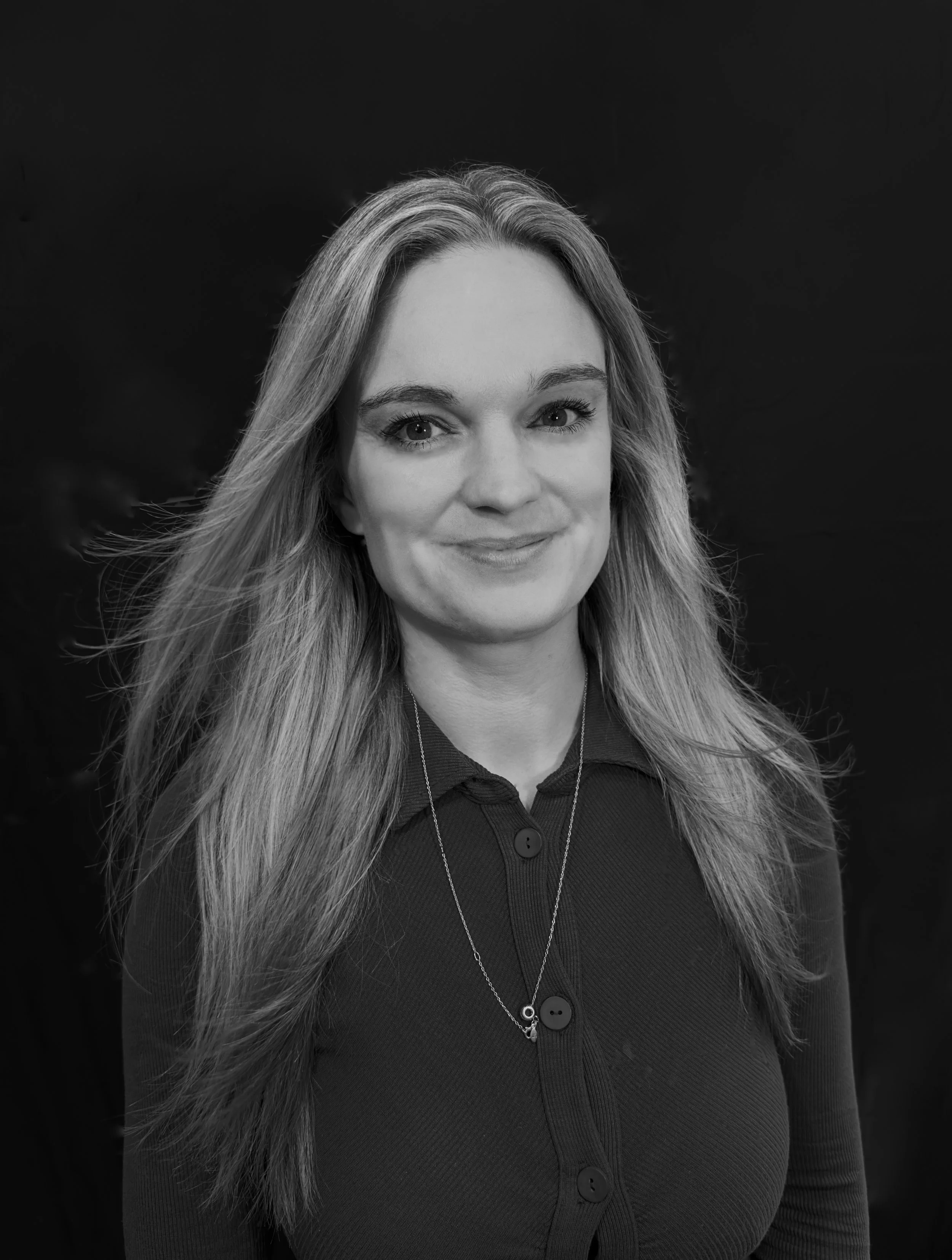 Woman with long hair smiling outdoors on a hill with city and water in the background, black and white photo.