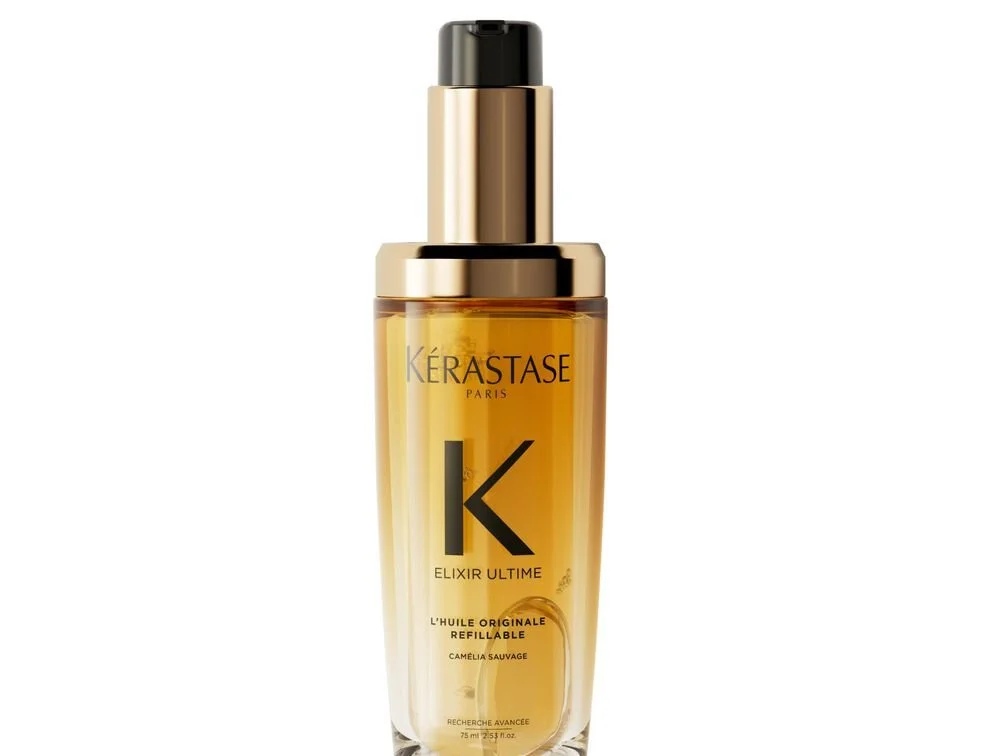 A bottle of Kérastase Paris Elixir Ultime hair oil with a black cap and gold lettering, in a transparent yellow-tinted bottle.
