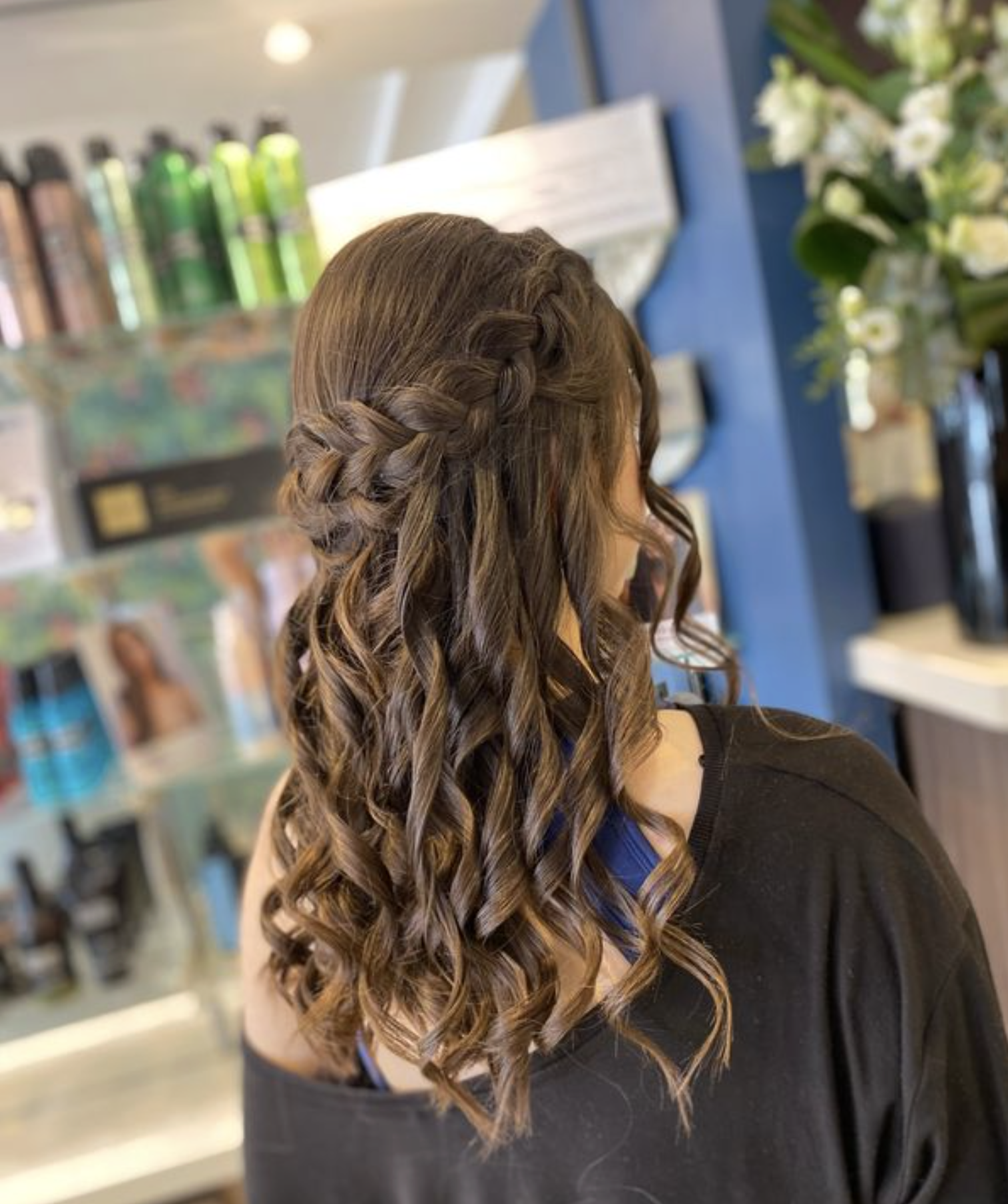 A woman with long, curly hair styled in a half-up, braided hairstyle.