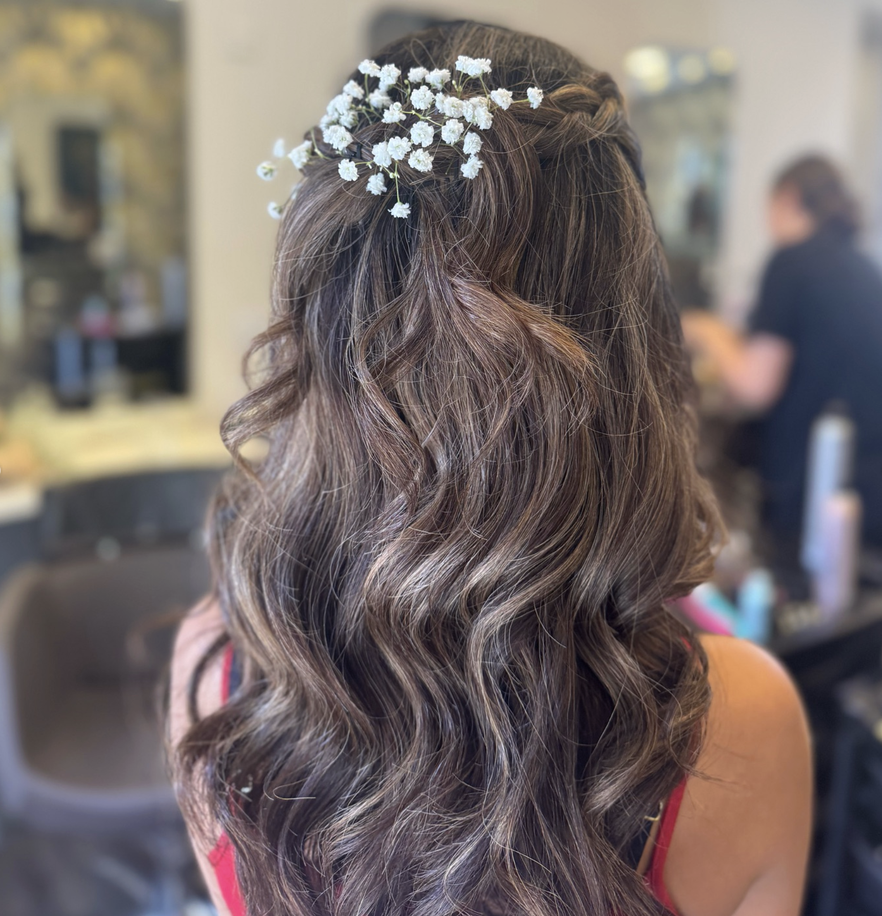 A woman with long, wavy brown hair decorated with small white flowers.