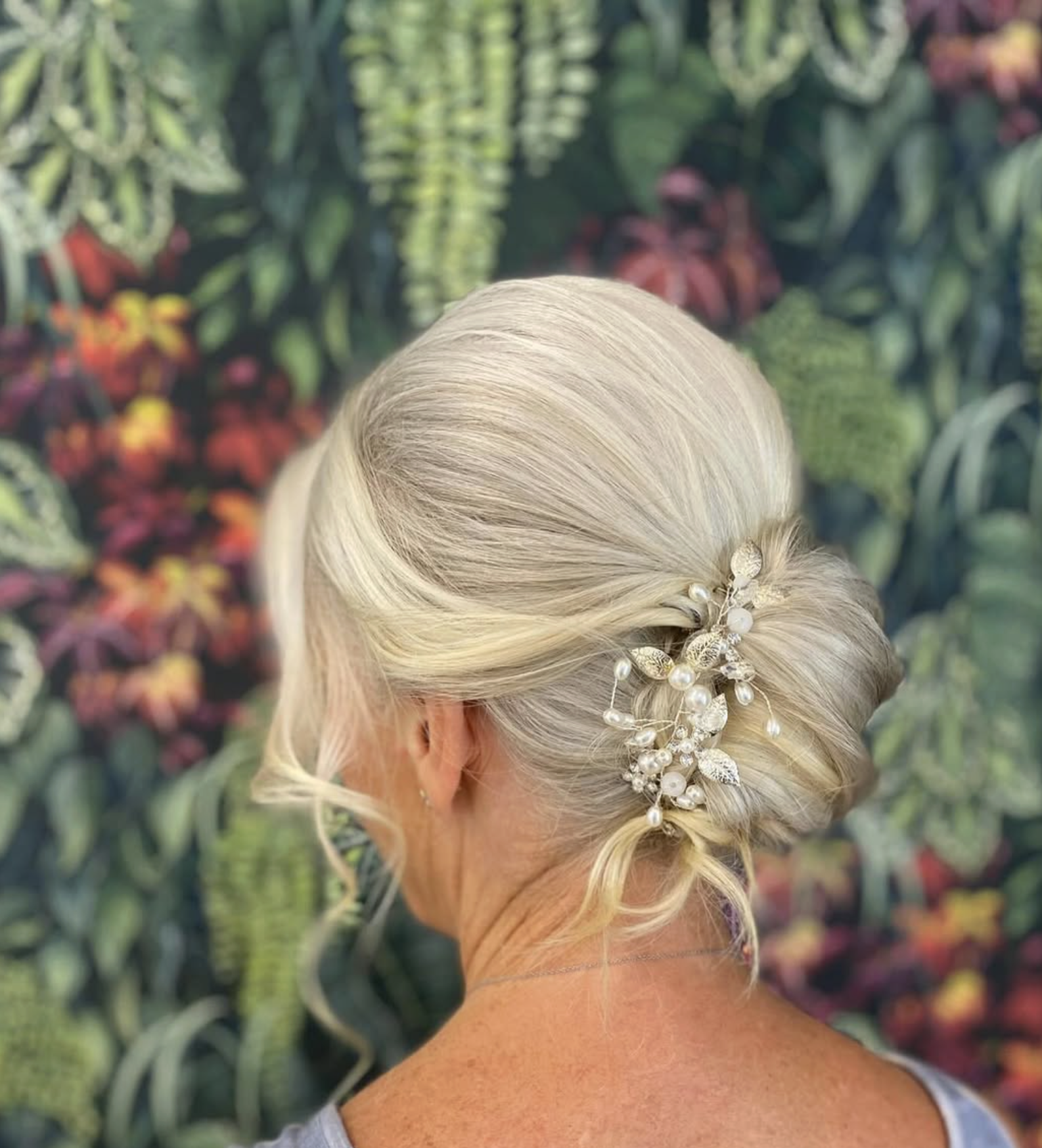 Elegant, styled hair with a decorative pearl and leaf hairpin, set against a leafy, floral background.