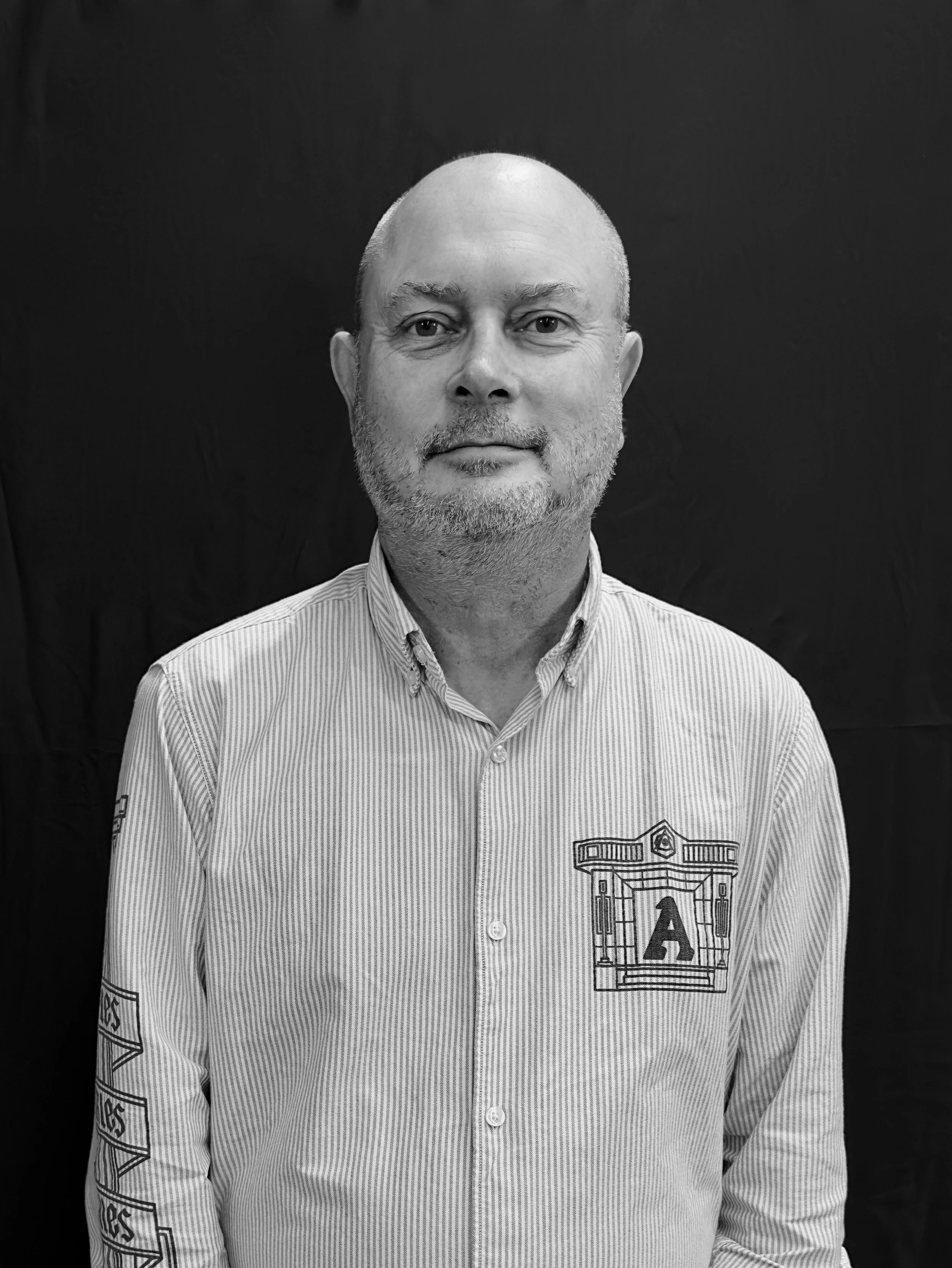 A man with a beard and short hair smiling in front of a wall with modern geometric decorations.