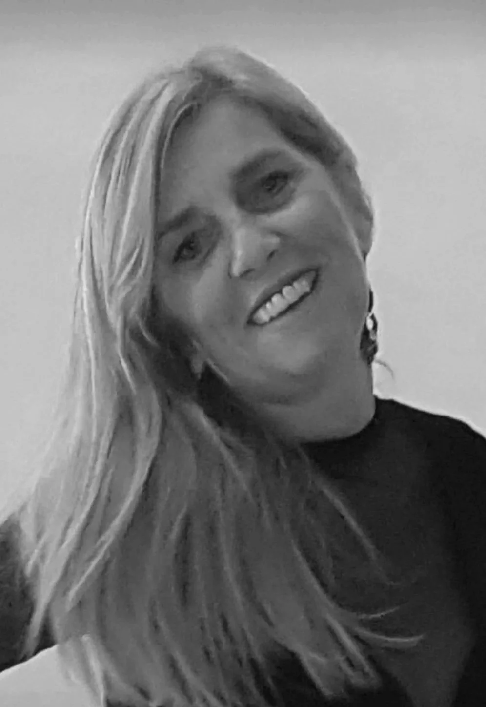 Black and white photo of a smiling woman with long, wavy hair and earrings.