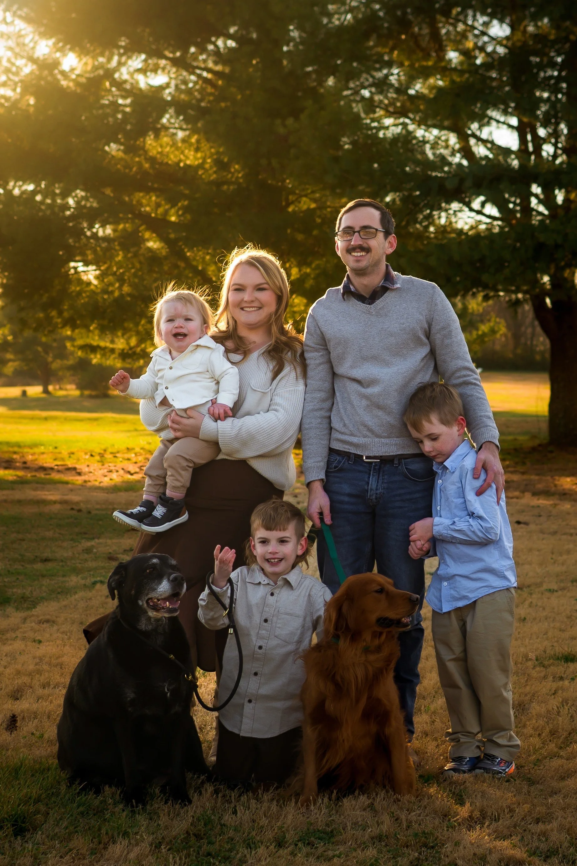 Photo of a mom, dad, and 3 young boys with 2 dogs in a field in Clarksville TN