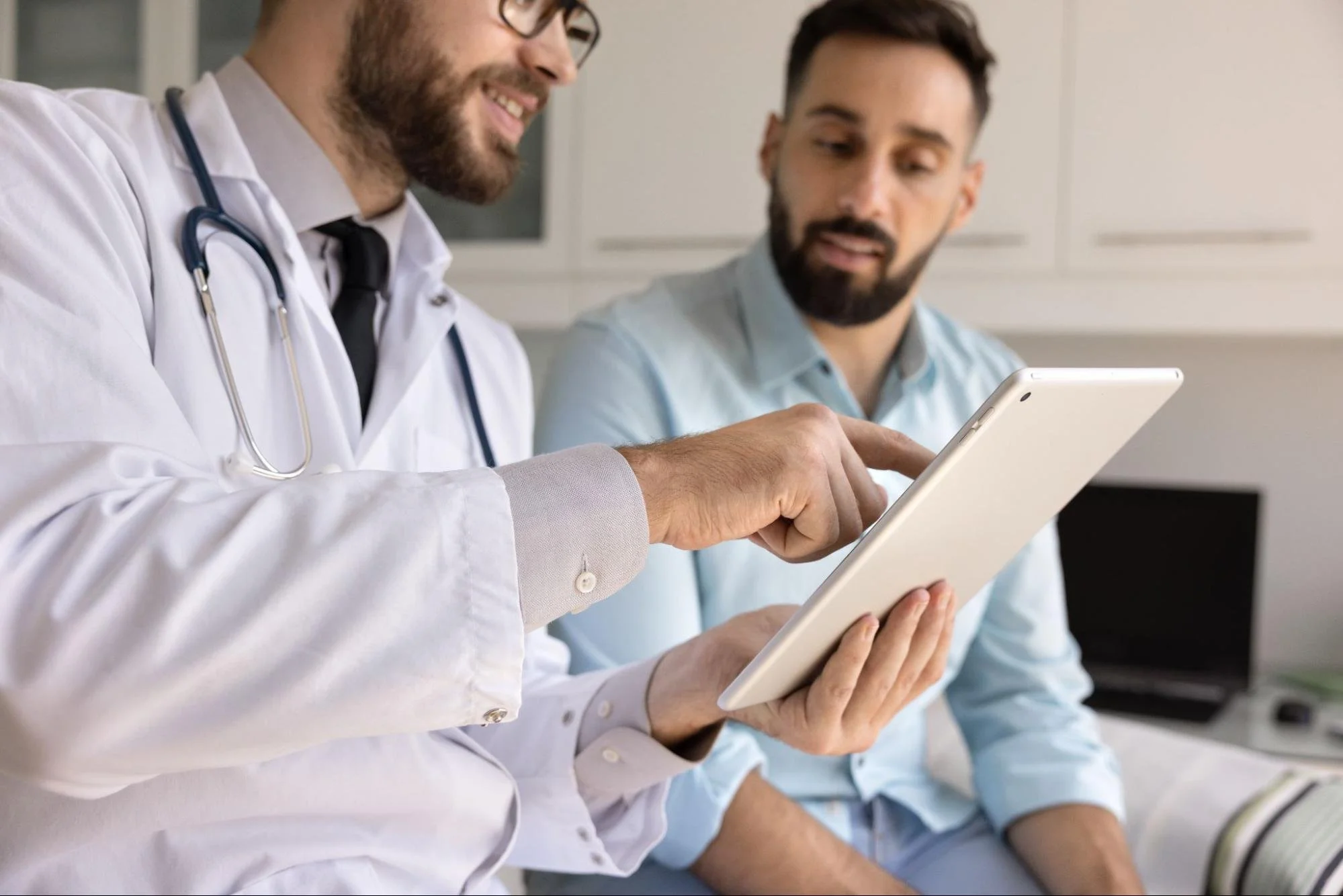 Doctor pointing at a tablet screen while discussing medical info with a male patient