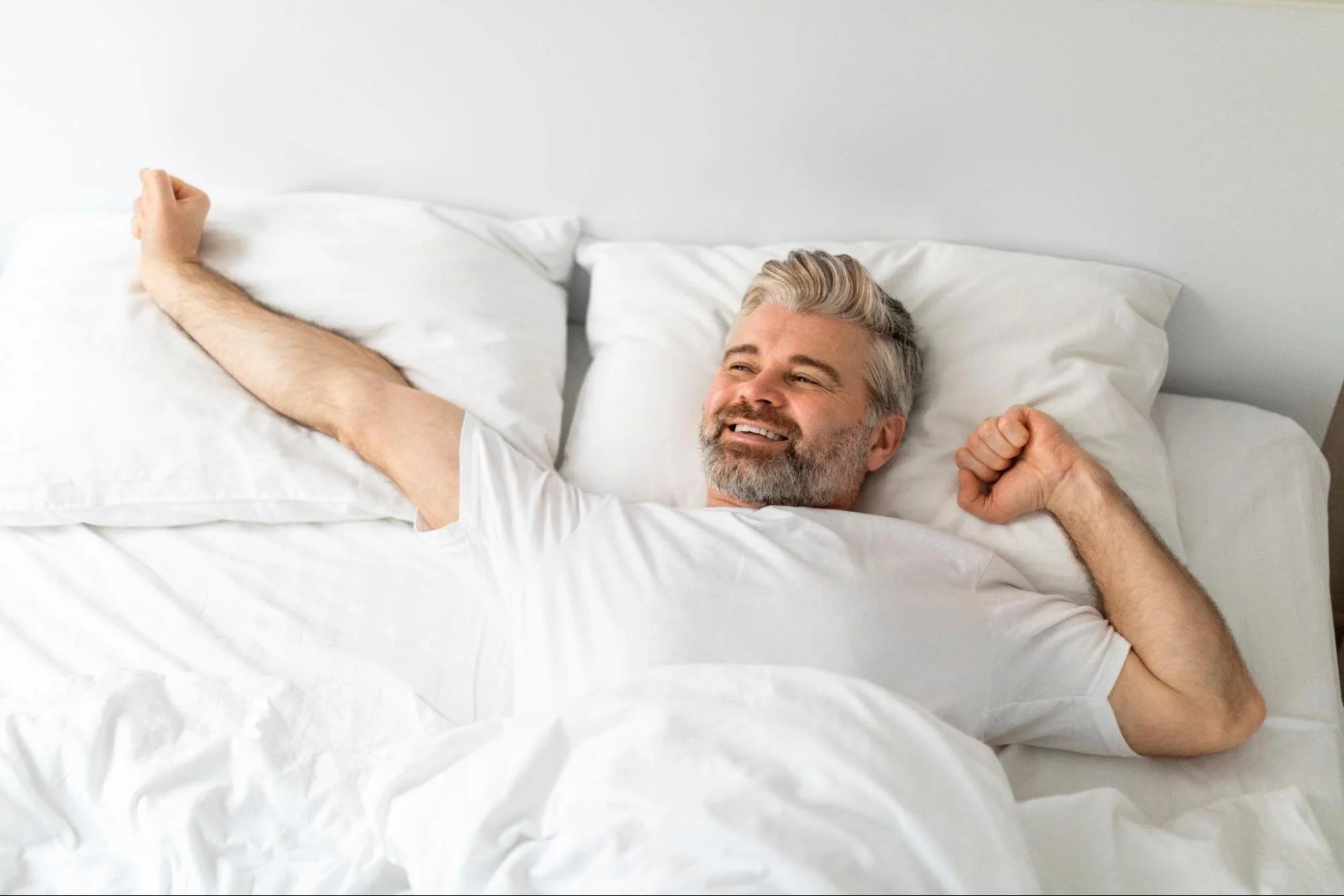 Middle-aged man waking up comfortably in bed and stretching his arms