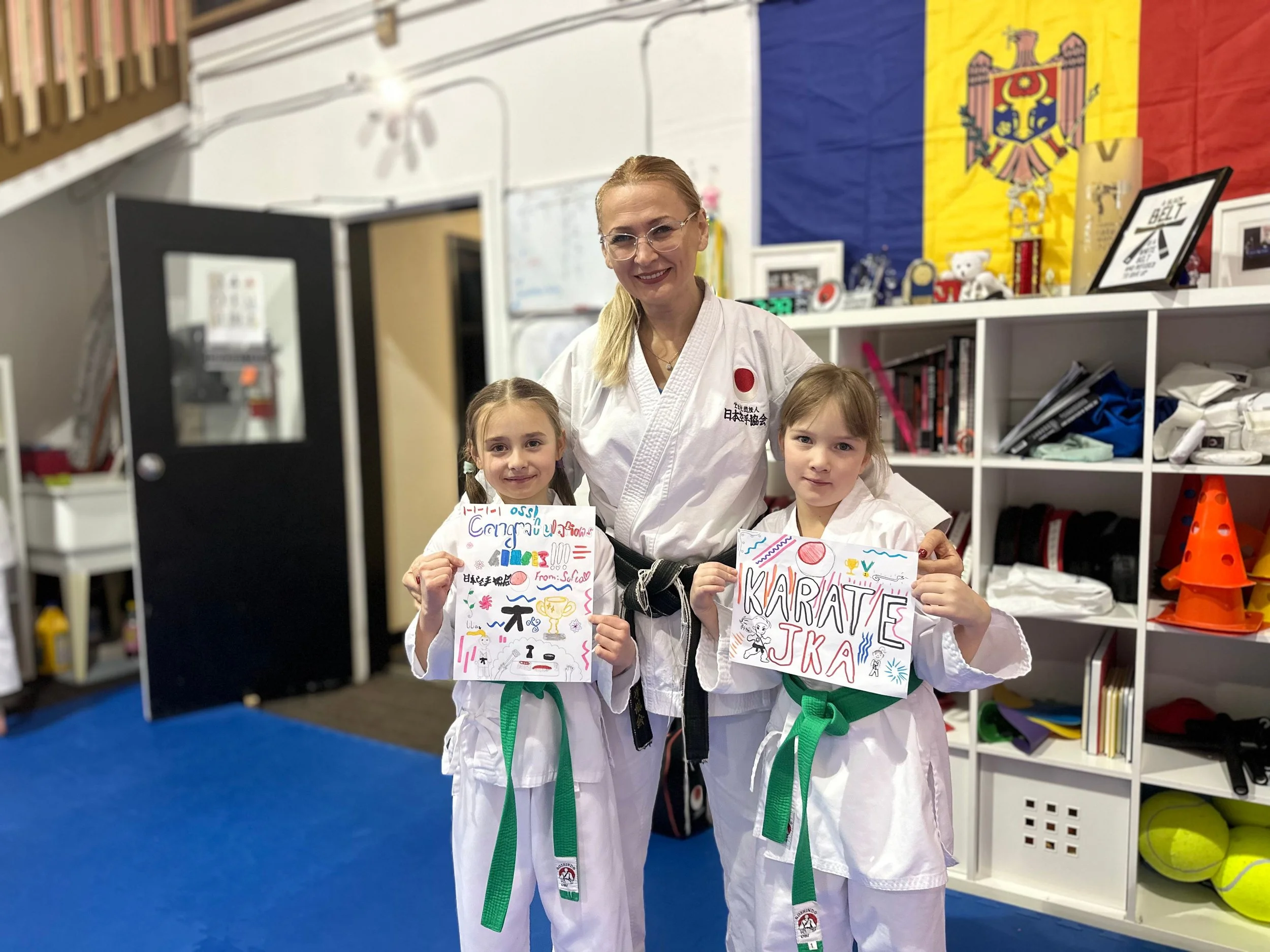 Group of children in white martial arts uniforms stretching on a blue and red mat in a dojo.