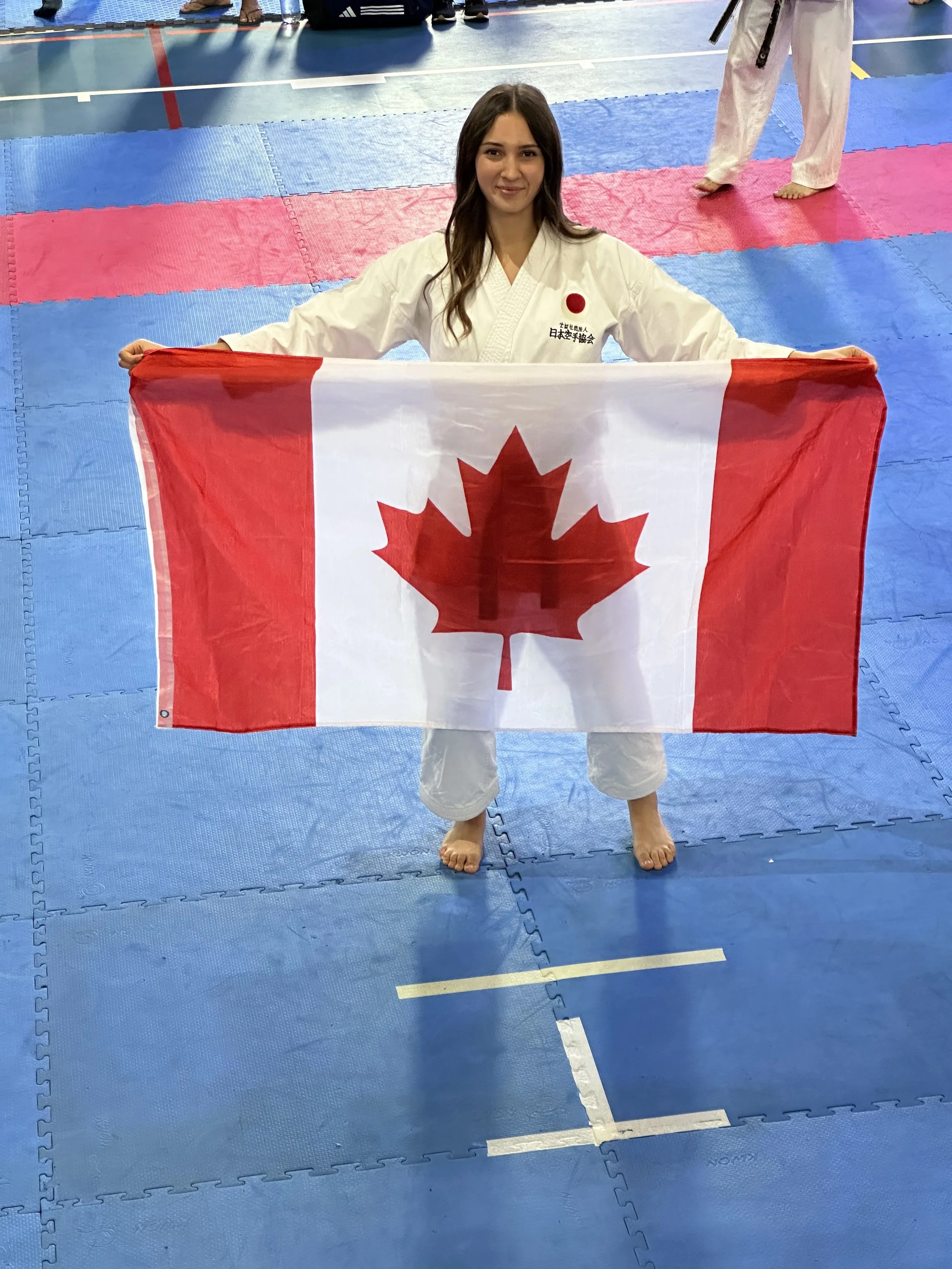Two people in martial arts attire sparring in a competition with an audience in the background.
