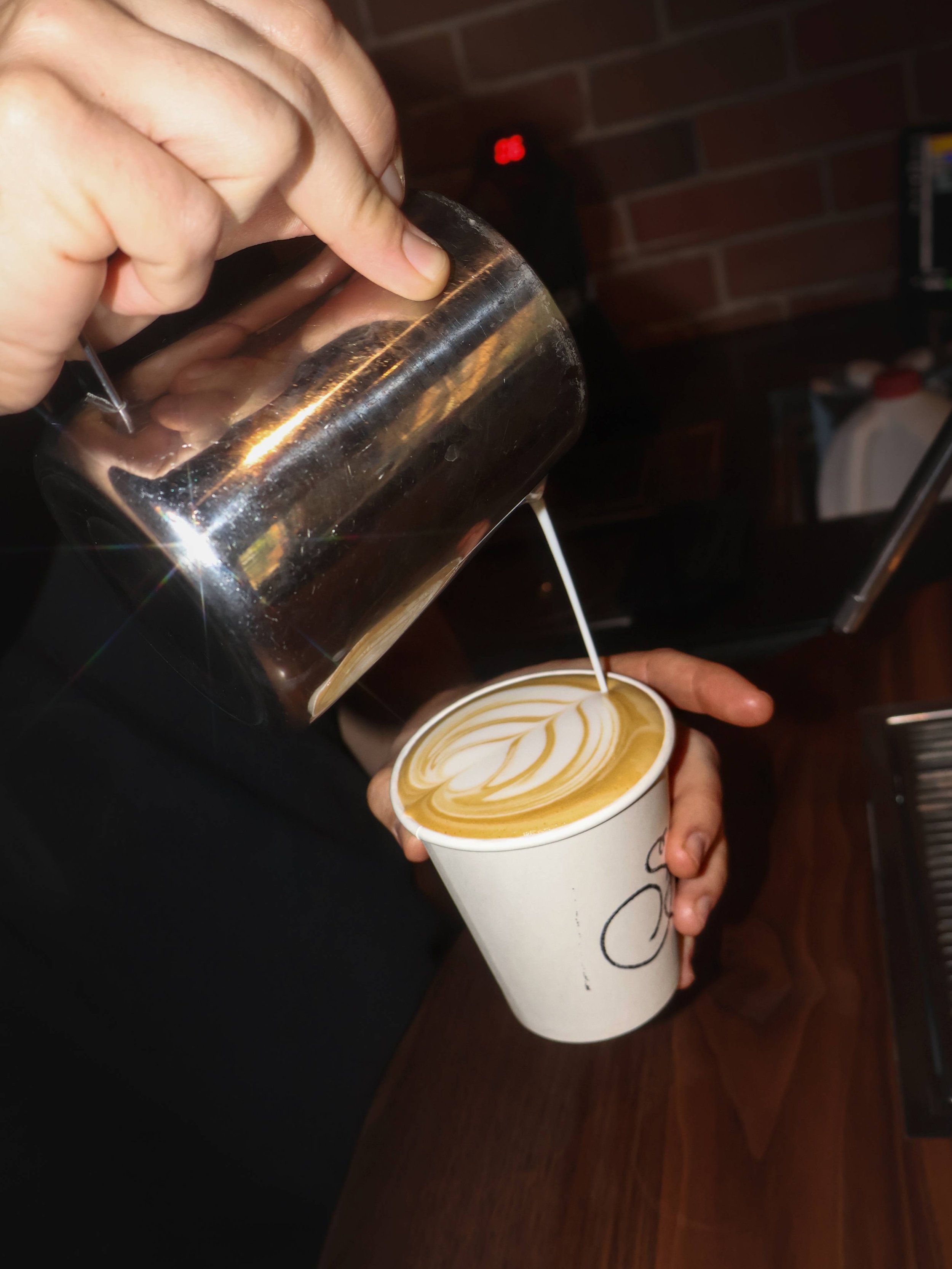 Barista pouring steamed milk into a cup of espresso to make a latte with latte art.