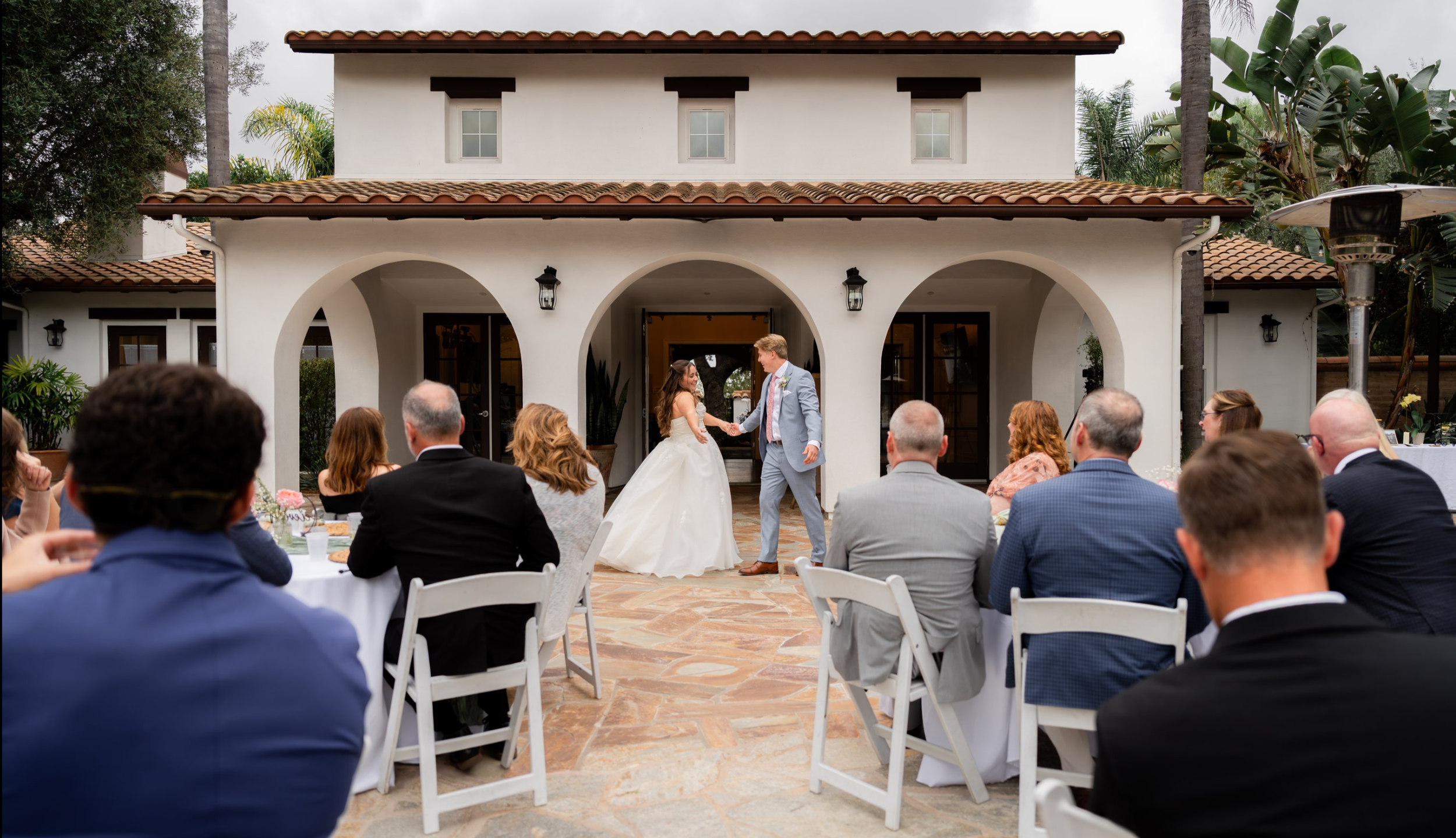 A bride and groom dancing during their wedding ceremony in an outdoor courtyard with guests watching.