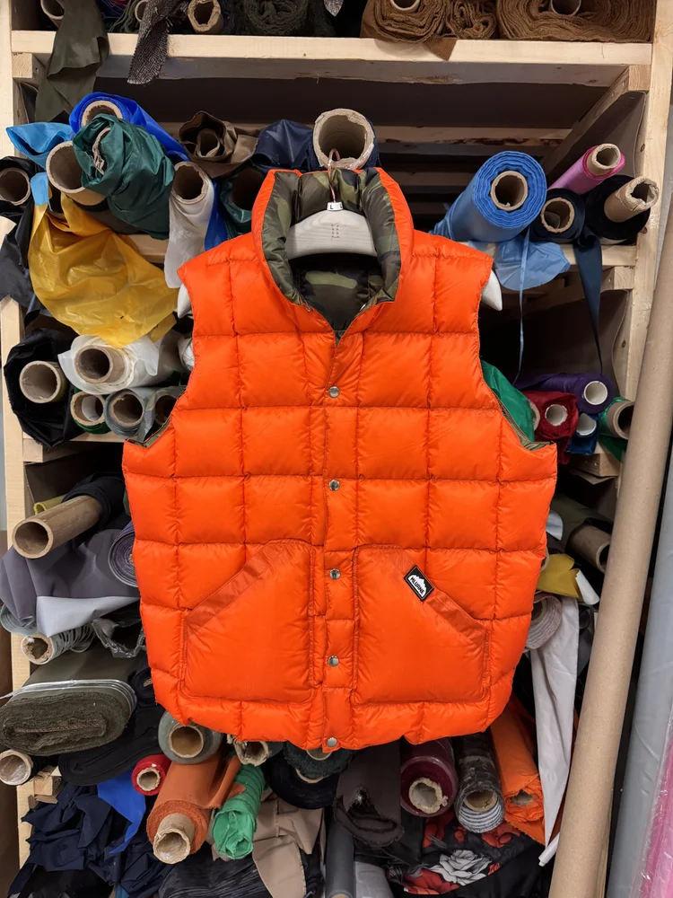 Orange Kluane down vest hanging in front of fabric rolls