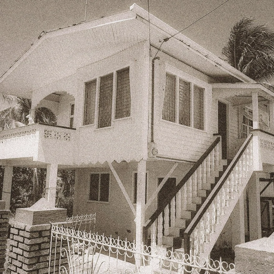 Two-story white house with stairs leading to the upper entrance, lattice windows, and decorative white iron fence in front.