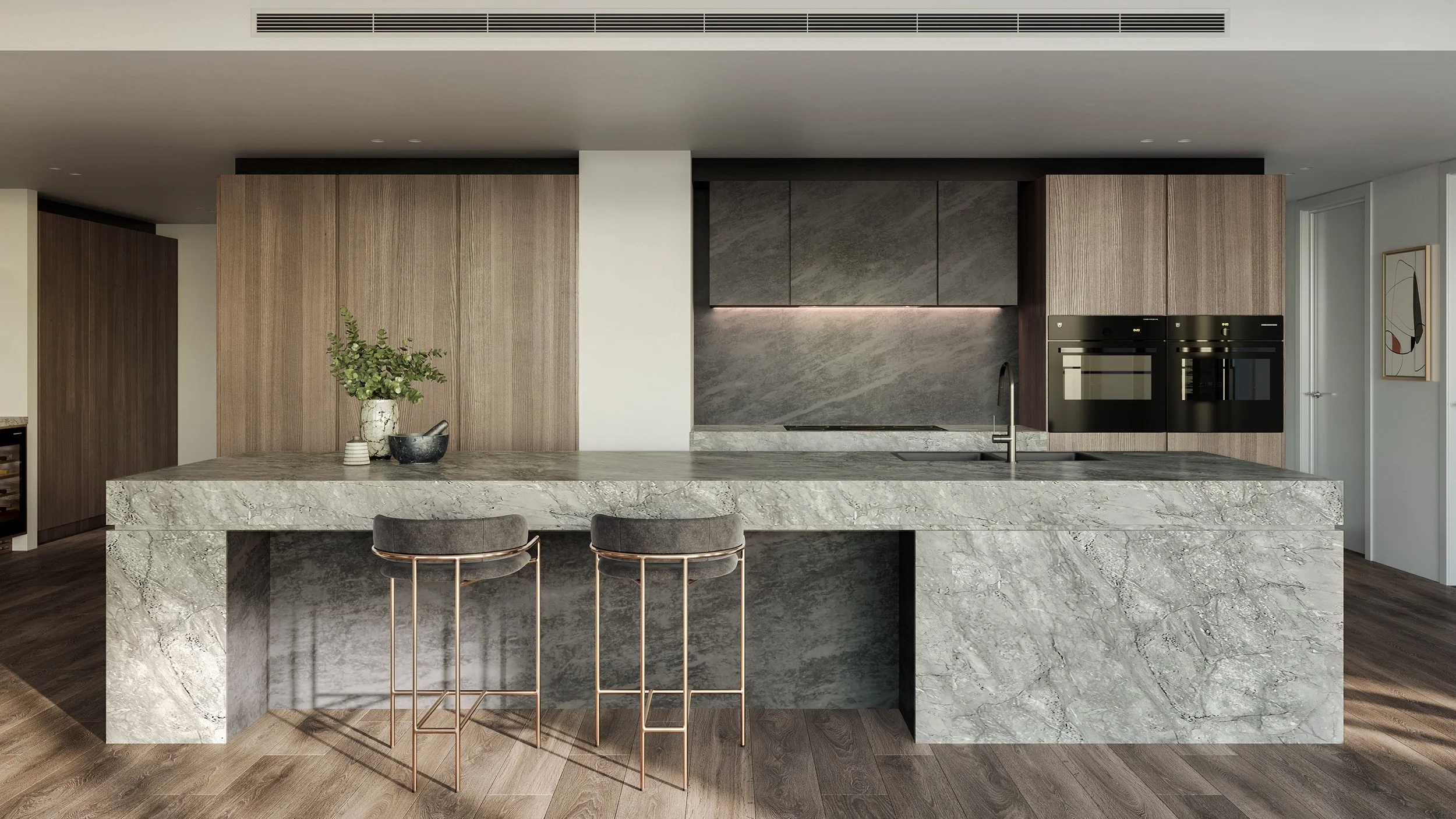 Modern kitchen with a marble island, wooden and dark gray cabinets, two bar stools, a vase with green foliage, and built-in ovens.