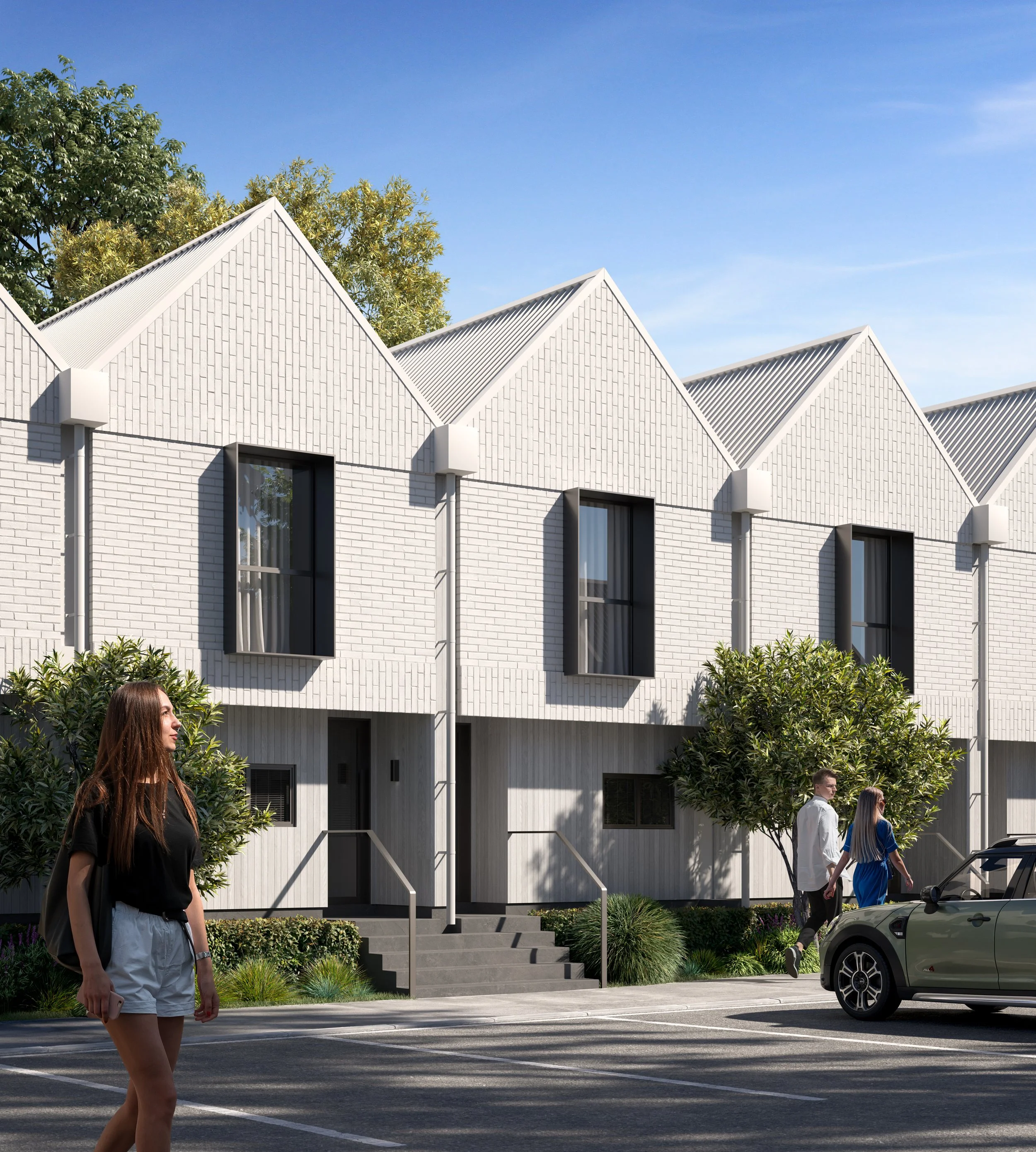 Modern white townhouse complex with two stories, featuring tall black windows, surrounded by greenery and trees, with a parking lot in front, and people walking nearby on a sunny day.