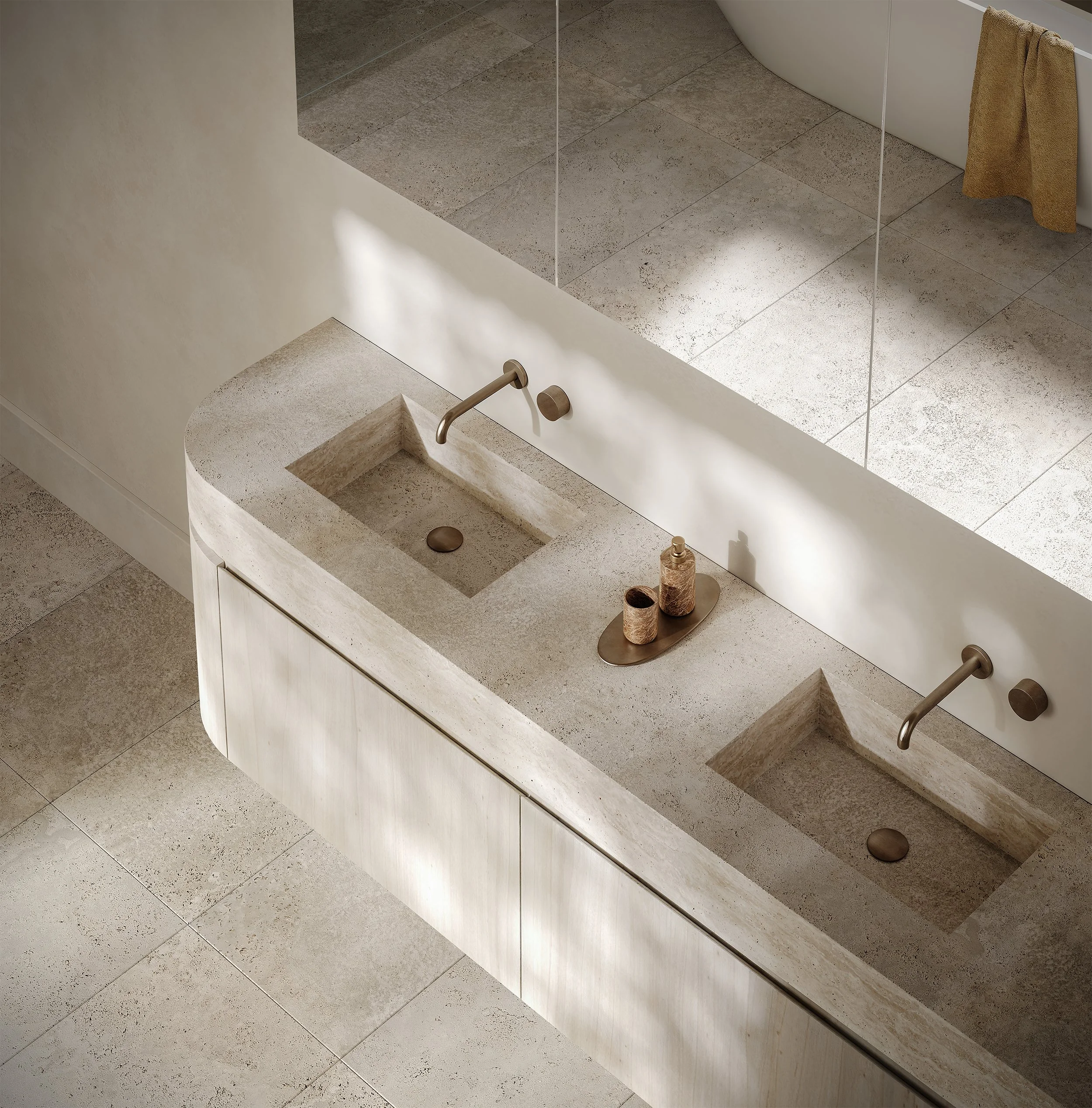 A modern double vanity bathroom with two integrated sinks, bronze fixtures, a large mirror, and neutral stone finish with subtle variations in color and texture.