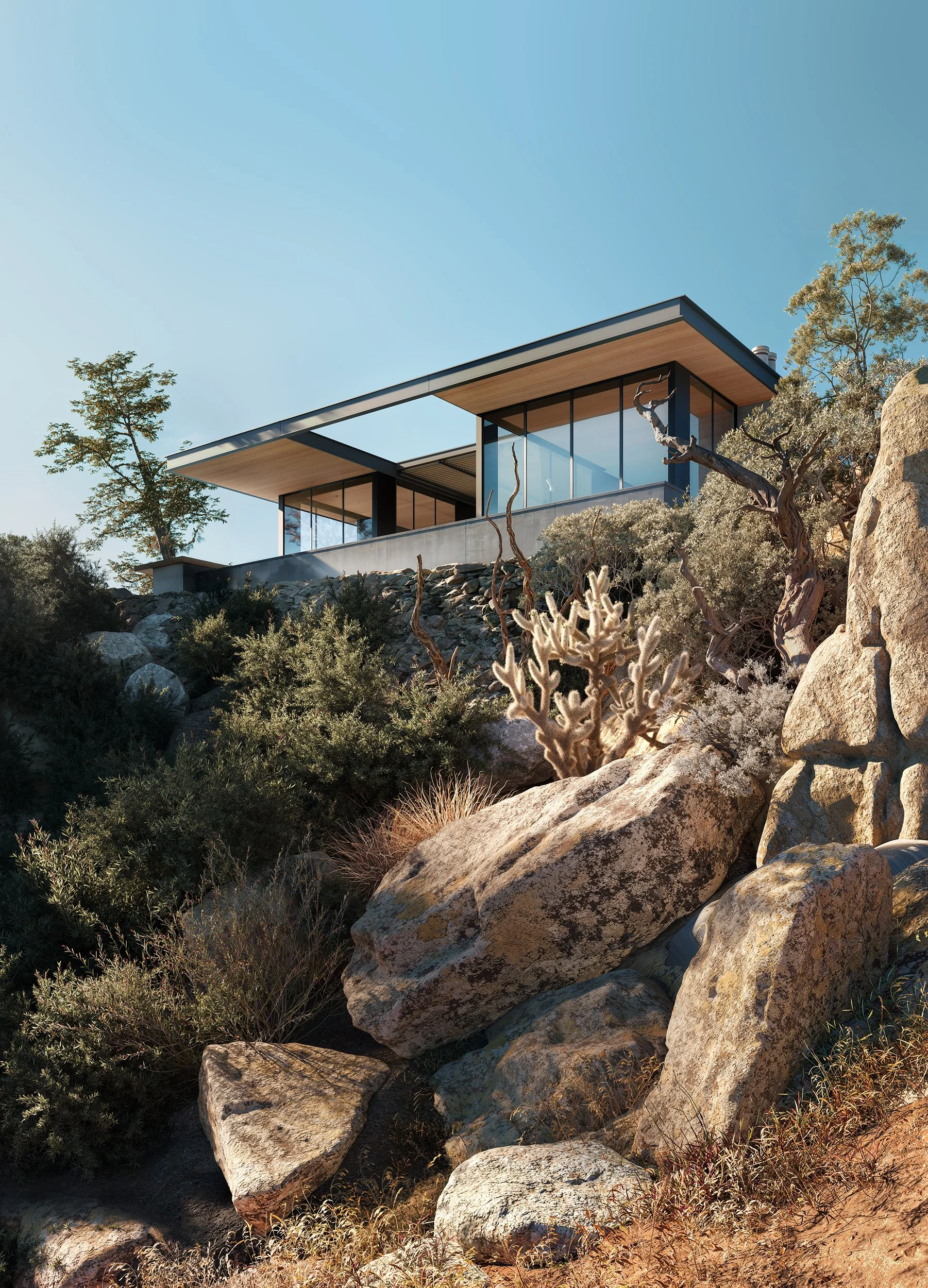 Modern house with large glass windows on a hillside surrounded by rocks and desert plants under a clear blue sky.