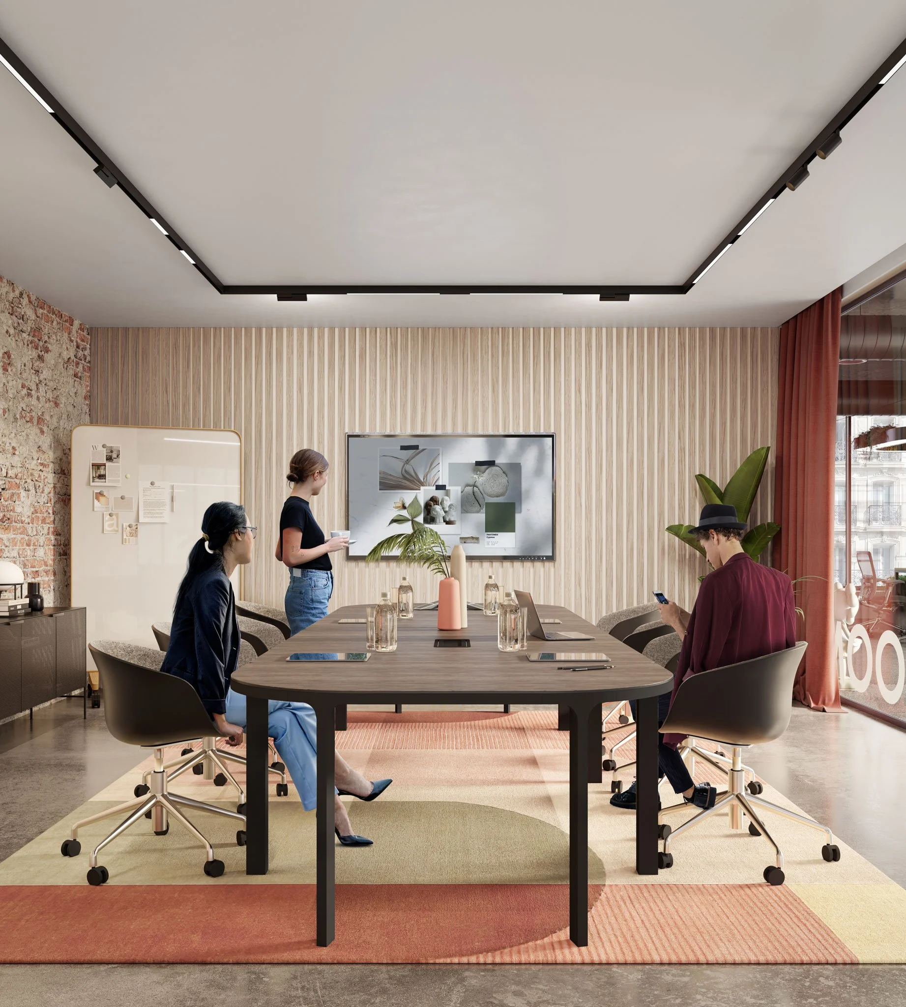 A modern conference room with three people, one standing and two seated, with a large digital screen on the wall, a wooden table, and various decorative elements including plants and a whiteboard.
