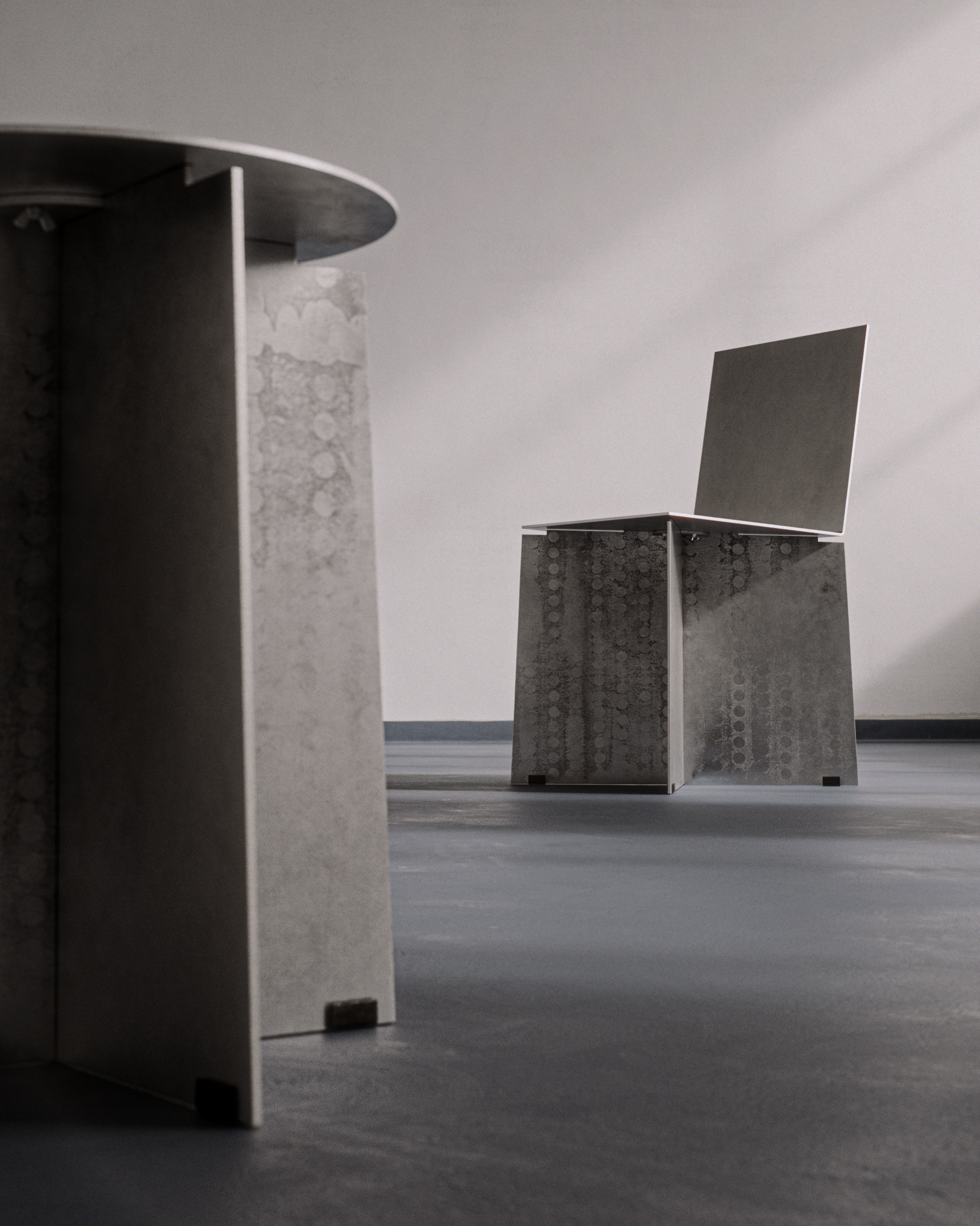Minimalist grey concrete desks on a grey floor, one with a laptop, in a neutral-lit room.