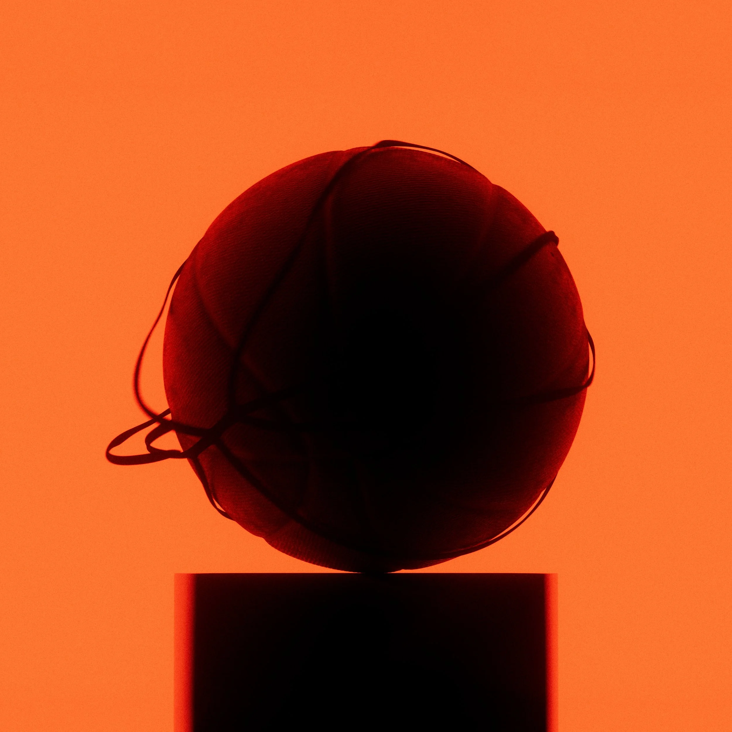A basketball rests on a minimalist pedestal, illuminated from below to create a warm glow and accentuate the texture and form of the ball.