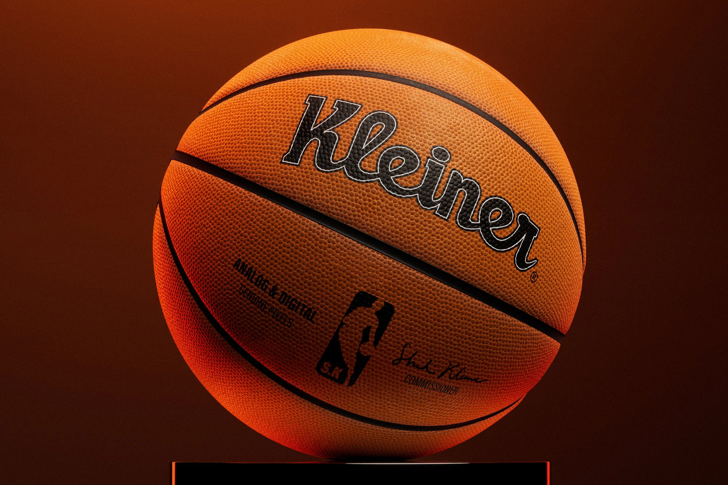 Studio Shoot. Advertisement. The image shows a basketball resting on a pedestal. The basketball is illuminated from below, casting a warm glow on its surface and creating an interesting light effect.