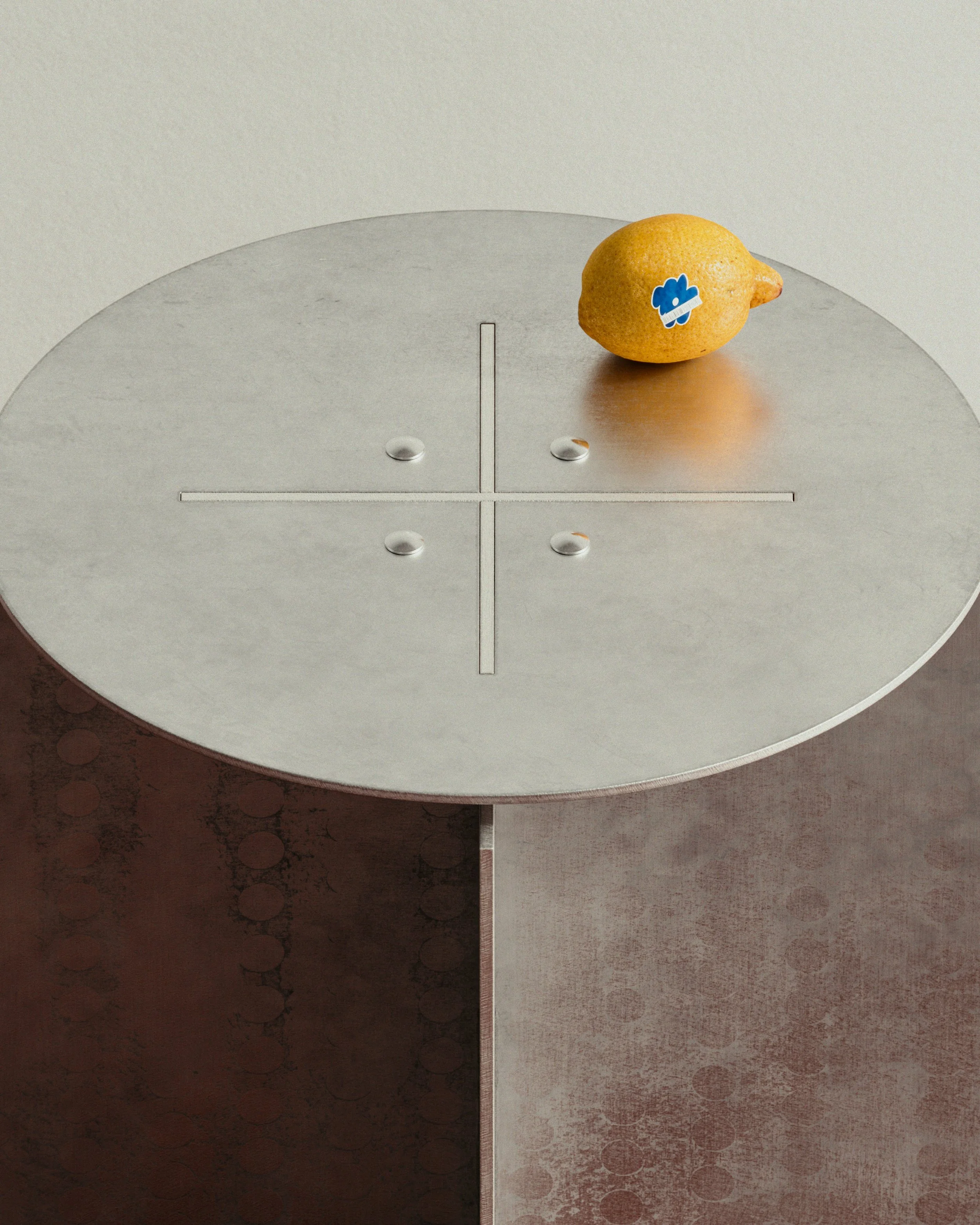 A puck on a round metallic air hockey table with a lemon and a sticker of a cloud on it.