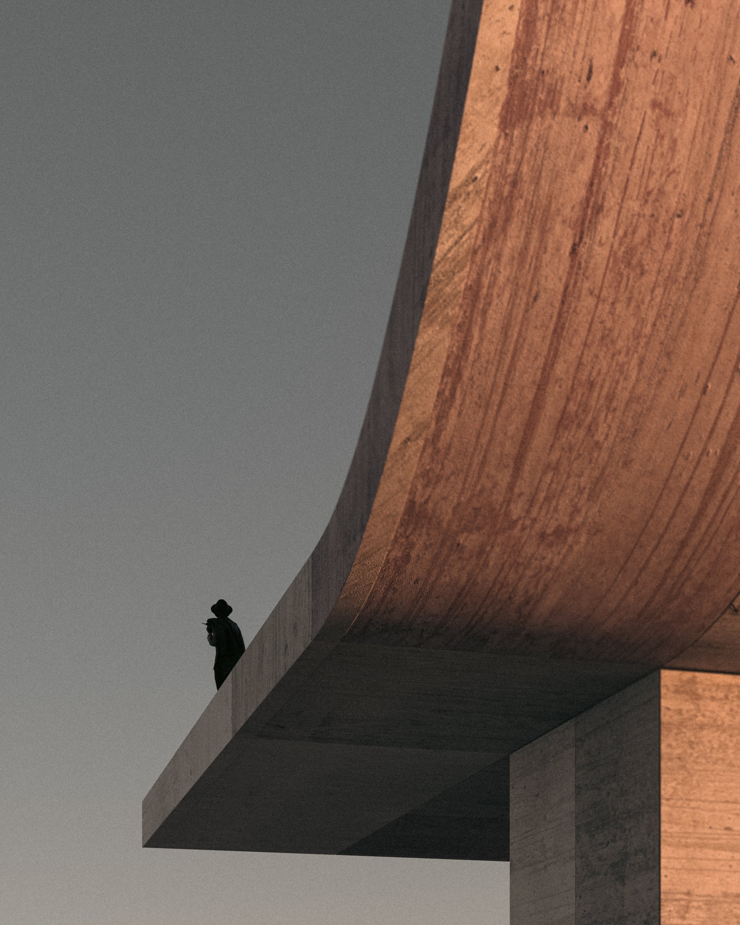 A person standing on an overhanging concrete ledge of a modern building at sunset, with a gray sky in the background.