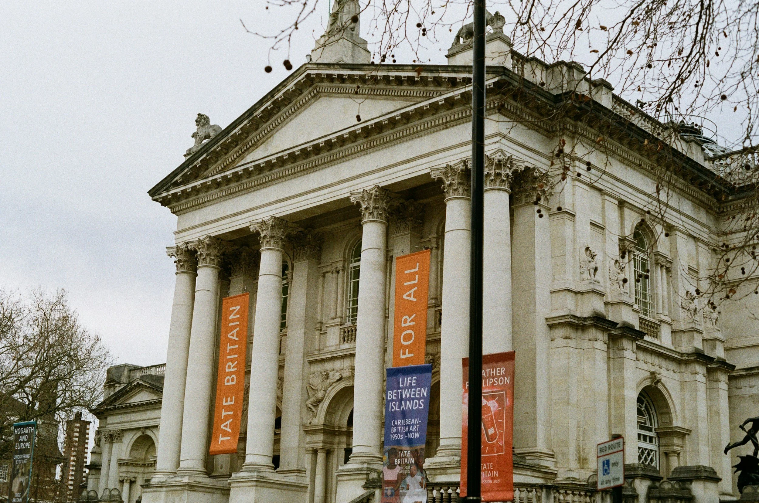 The Tate Britain art museum building with classical columns and banners displaying 'Tate Britain' and 'For All'.