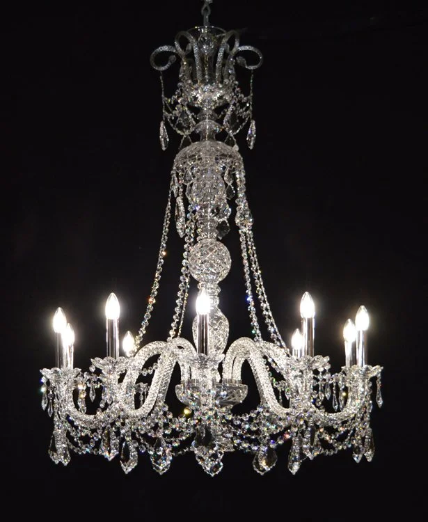 Sparkling crystal chandelier with multiple lit bulbs hanging against a black ceiling.