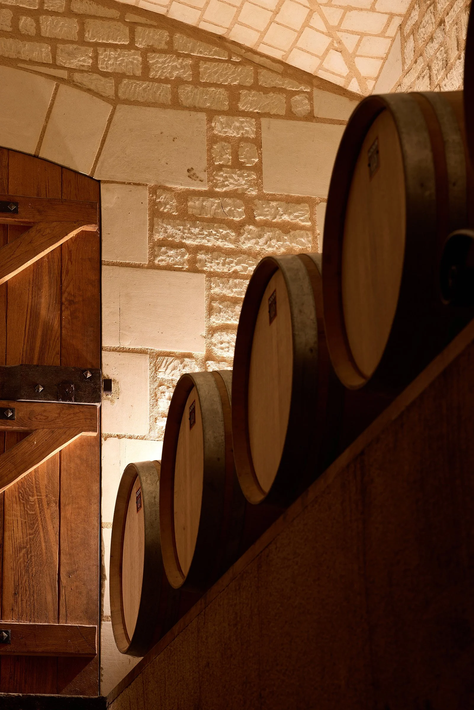 Chai de vinification du domaine de la Chapelle, avec des barriques dans l'ombre devant un mur de pierre blanche
