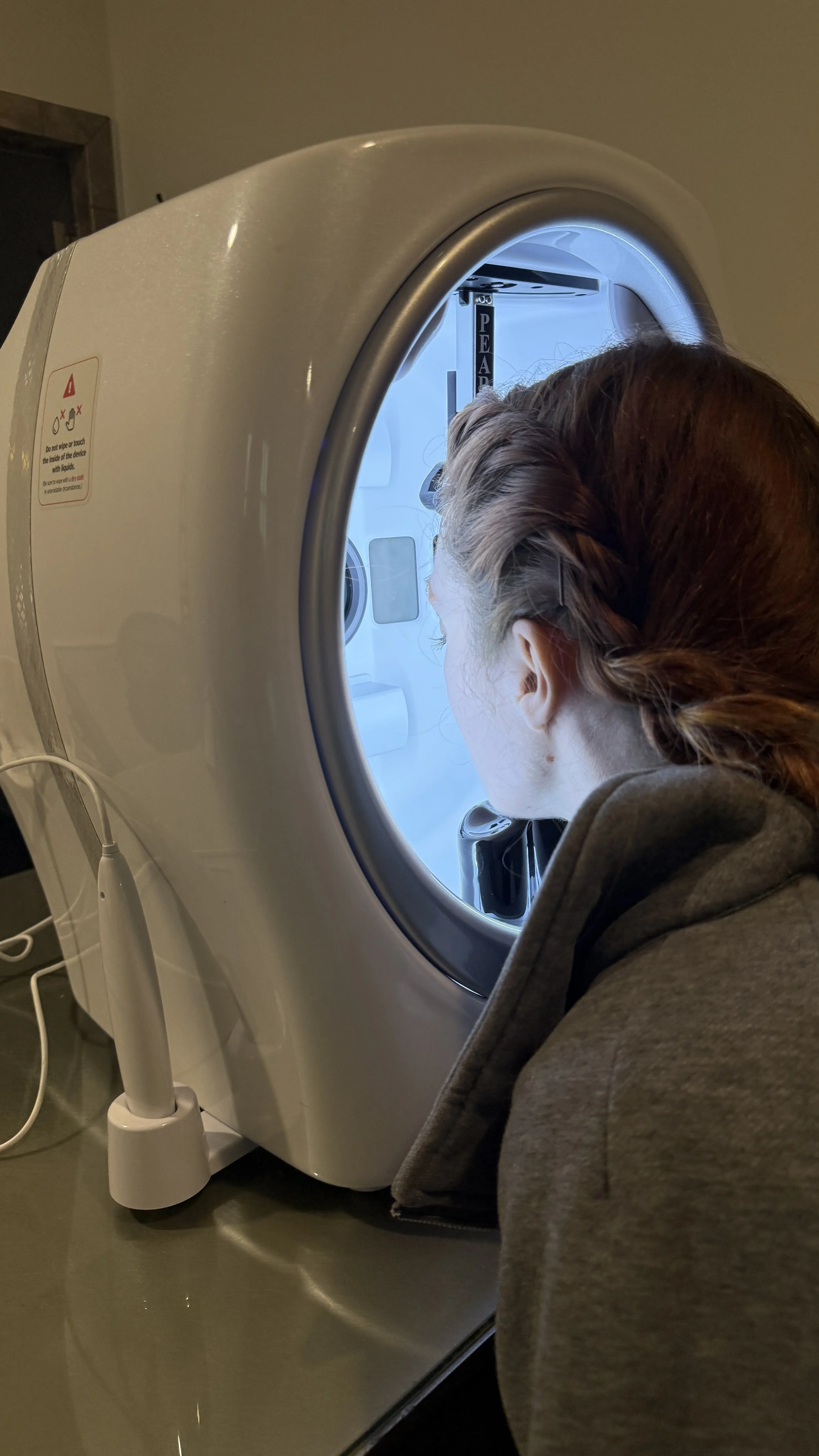 A person with braided hair looking into a CT scanner machine at a medical facility.