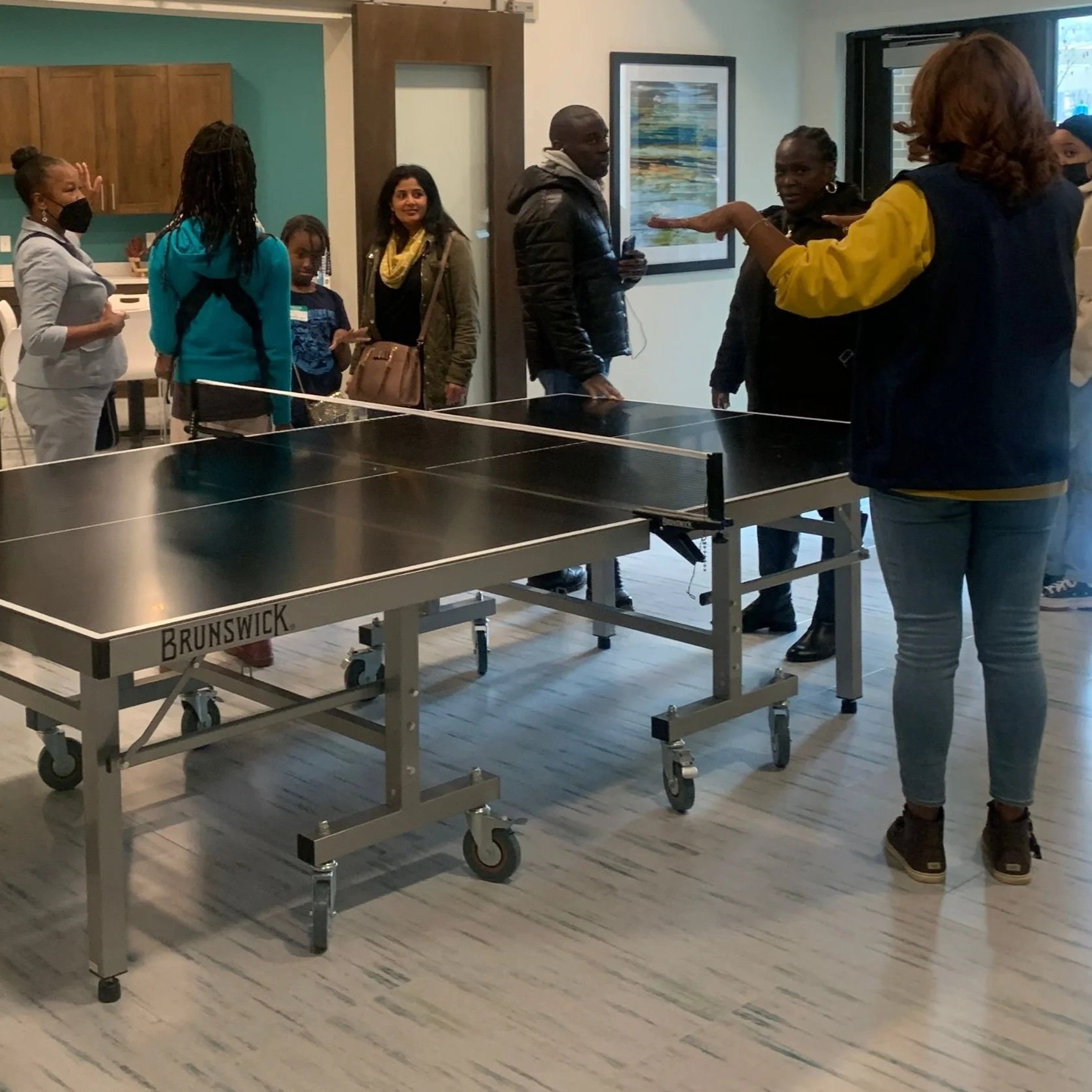 Residents and stakeholders gather indoors around a ping-pong table during a community engagement session related to the map amendment application for the Meadowbrook Run Apartments.