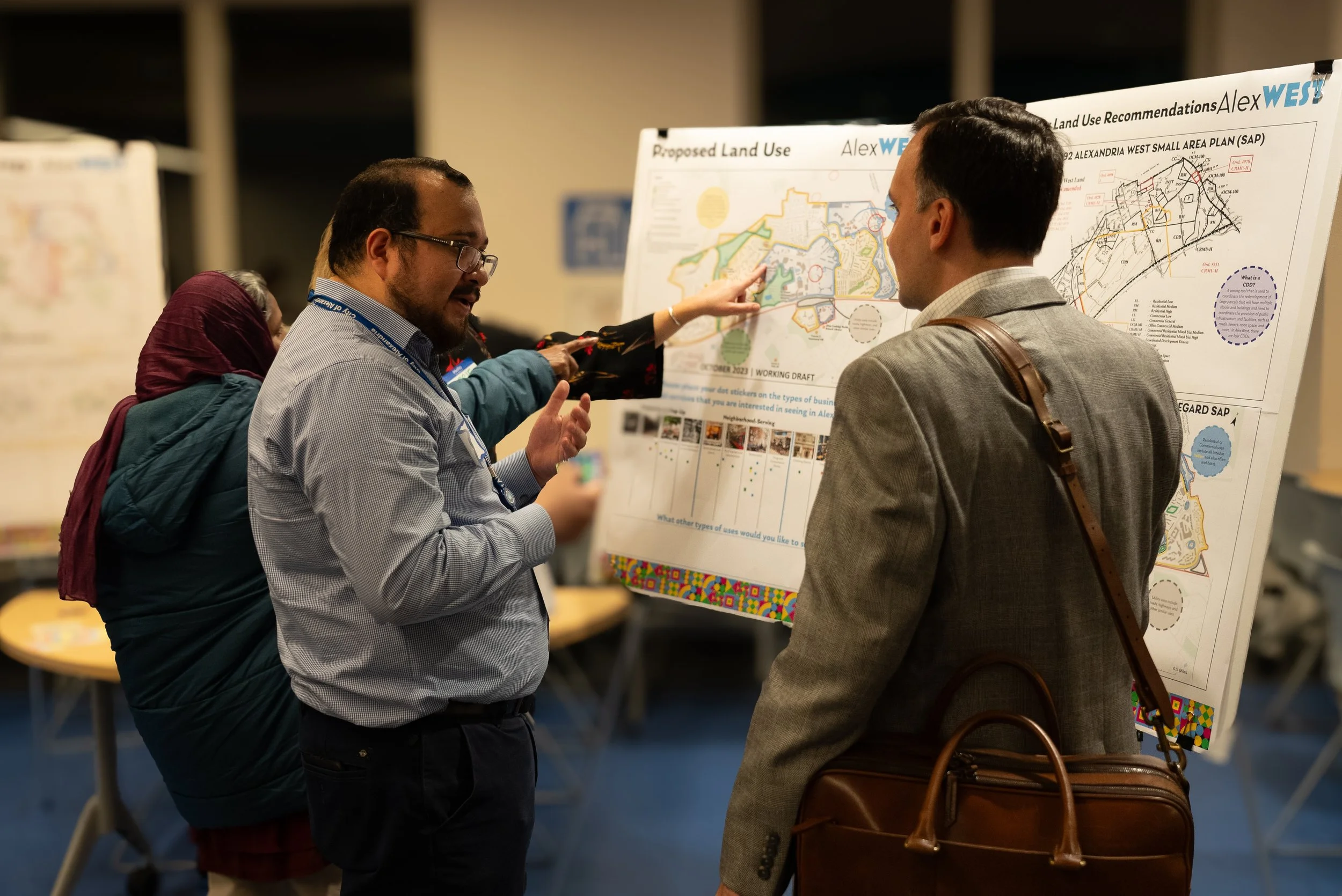 People discuss proposed land use plans at a public meeting, with maps and charts displayed on large posters.