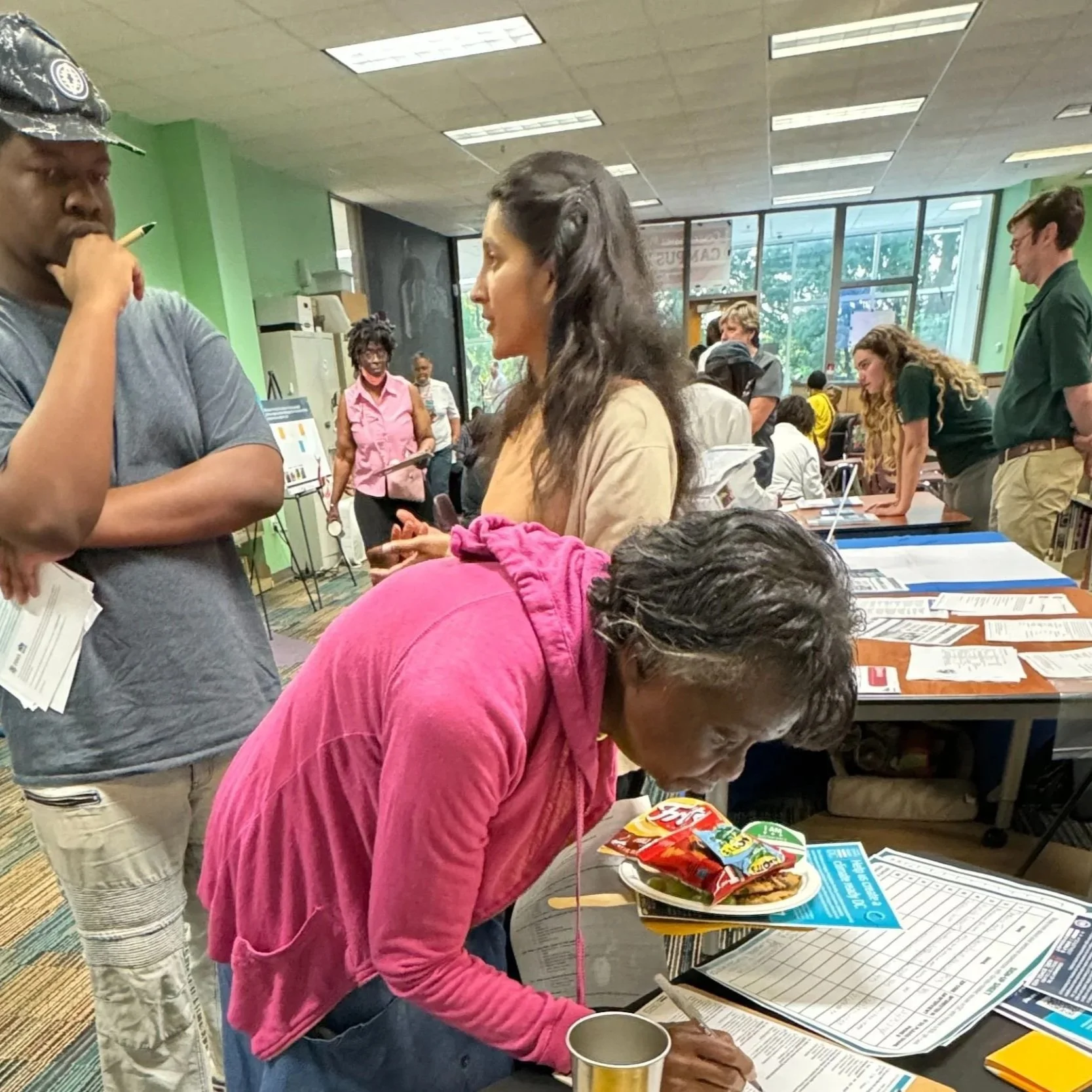 Community members gathered in a library space for a climate planning meeting, discussing ideas and reviewing informational boards and materials on tables.