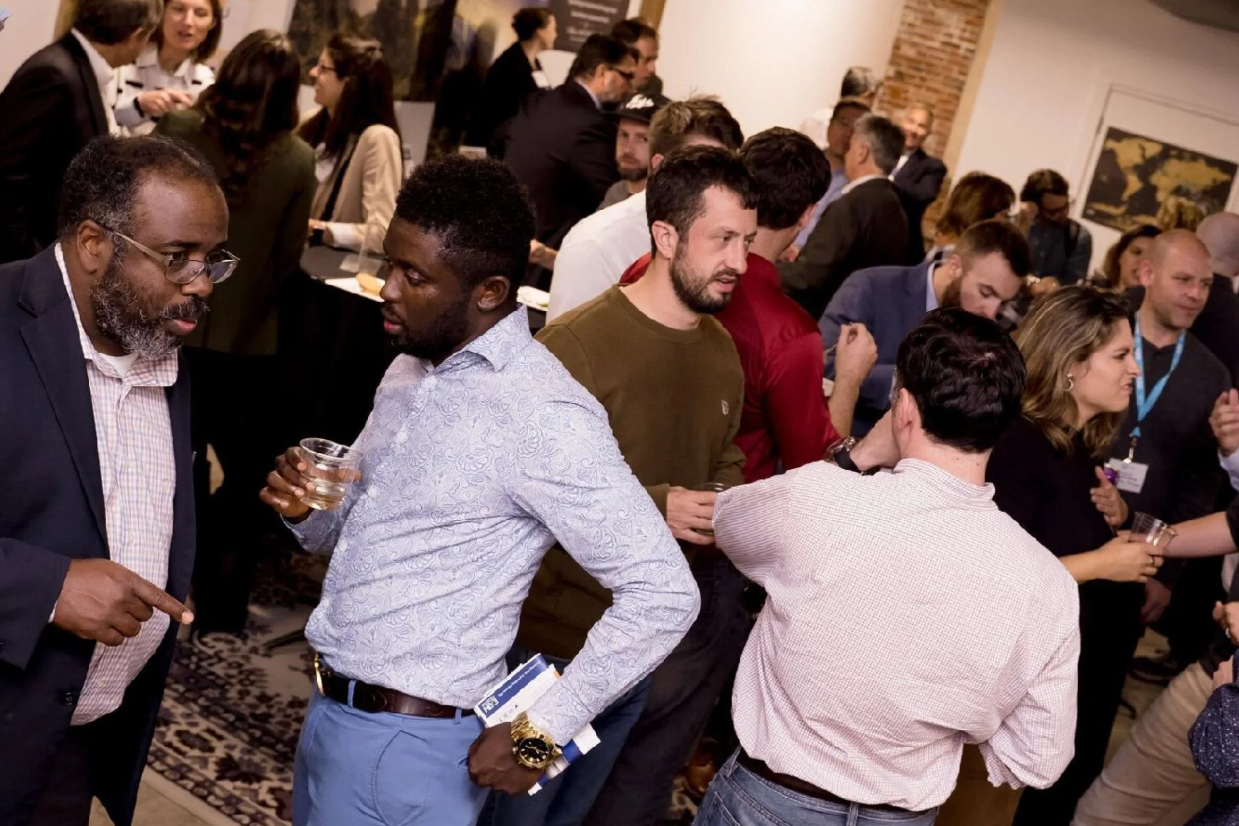 People gathered at a networking event, talking in small groups and holding drinks, with a busy room full of conversations during Baltimore Innovation Week.