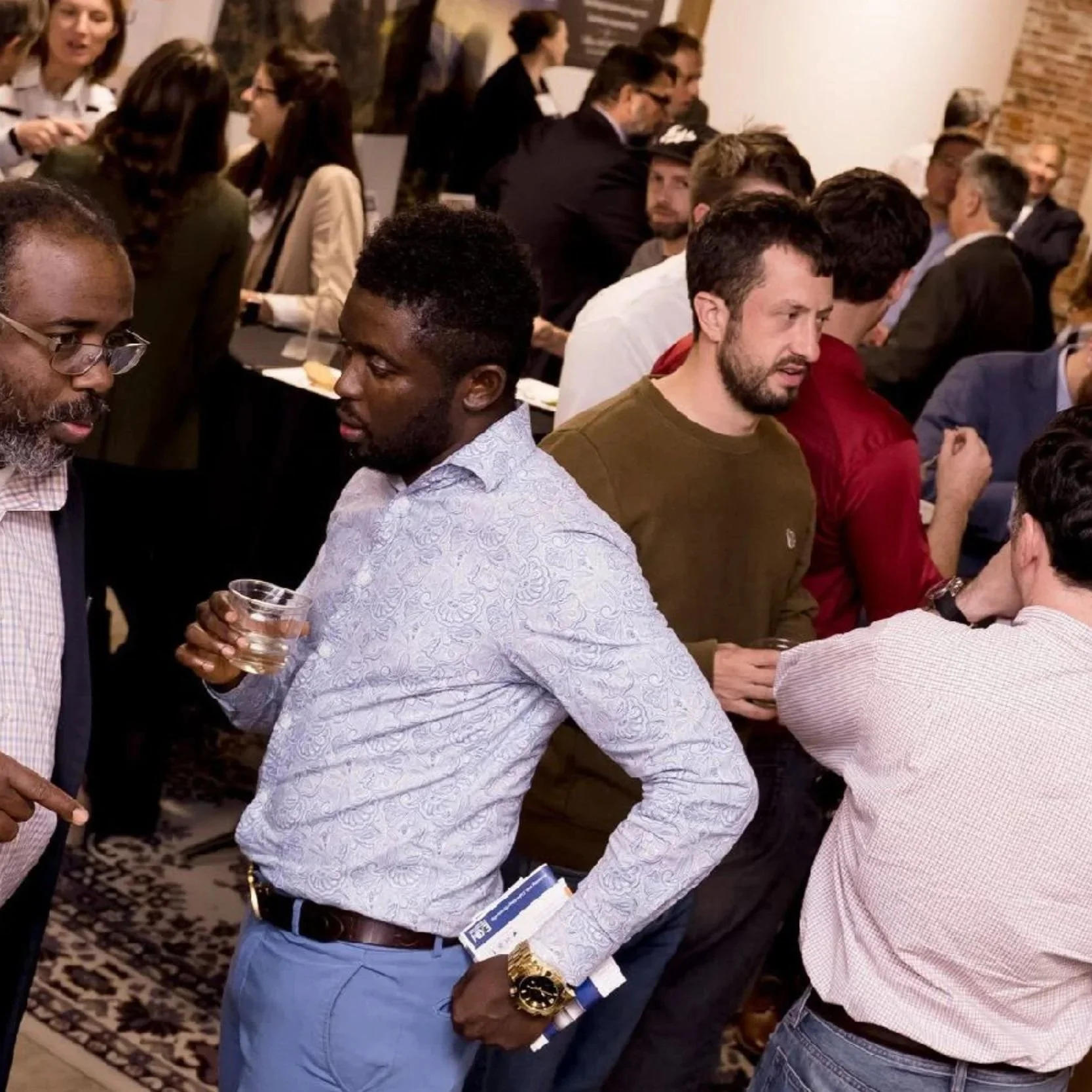 People gathered at a networking event, talking in small groups and holding drinks, with a busy room full of conversations during Baltimore Innovation Week.