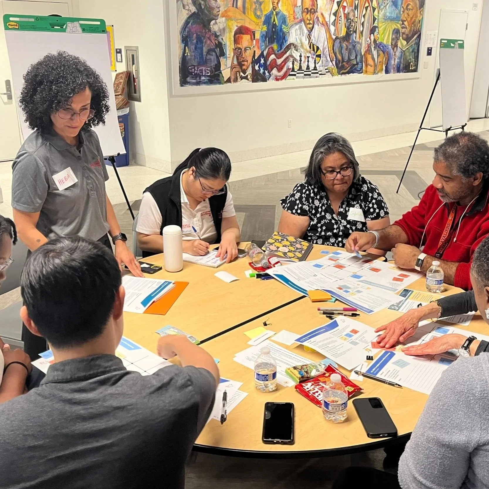 Community members gathered around a table during a master plan update meeting, discussing ideas and reviewing planning materials with maps and documents.