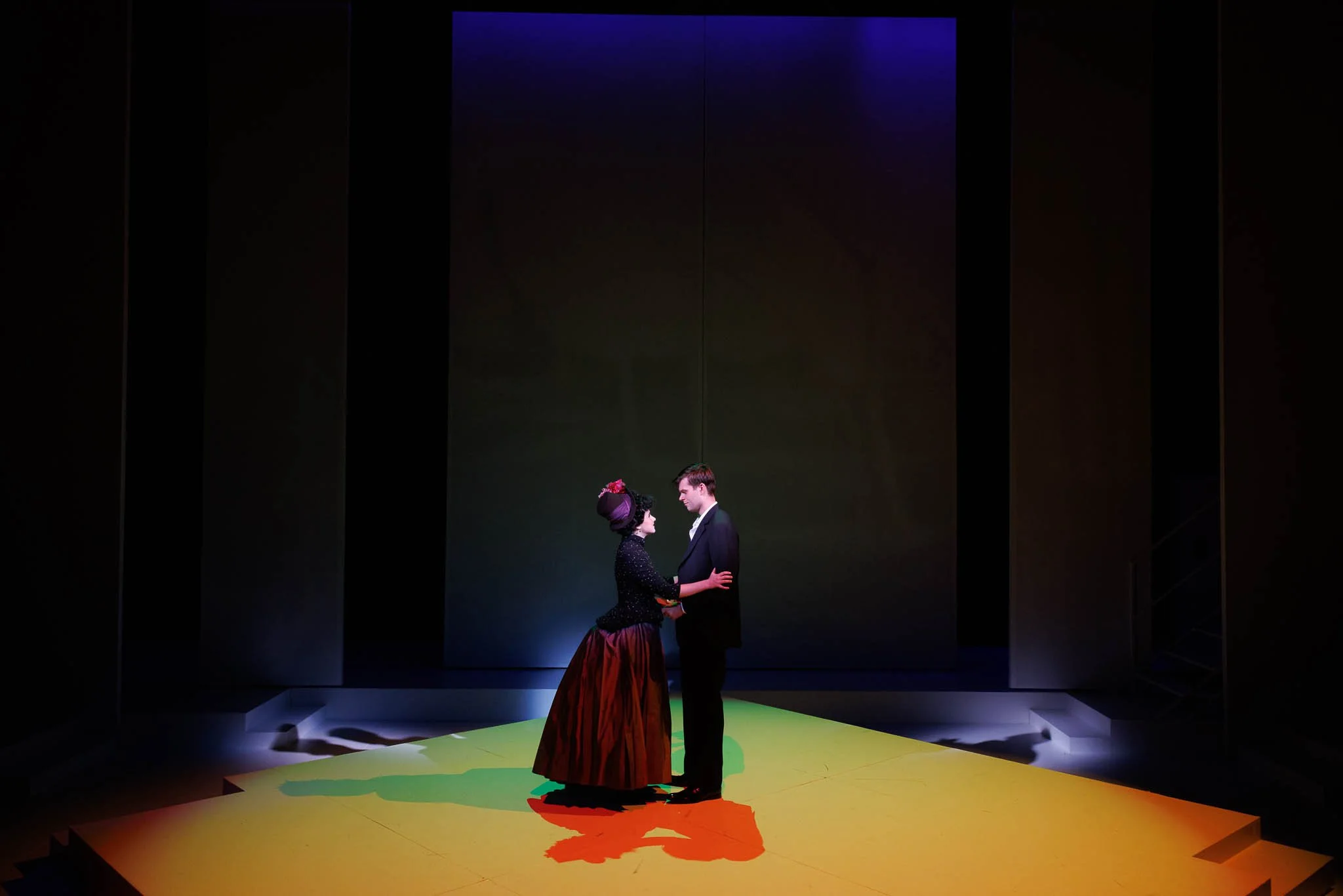 Two people dancing on a brightly lit stage in a theater, with a dark background and minimal set design.