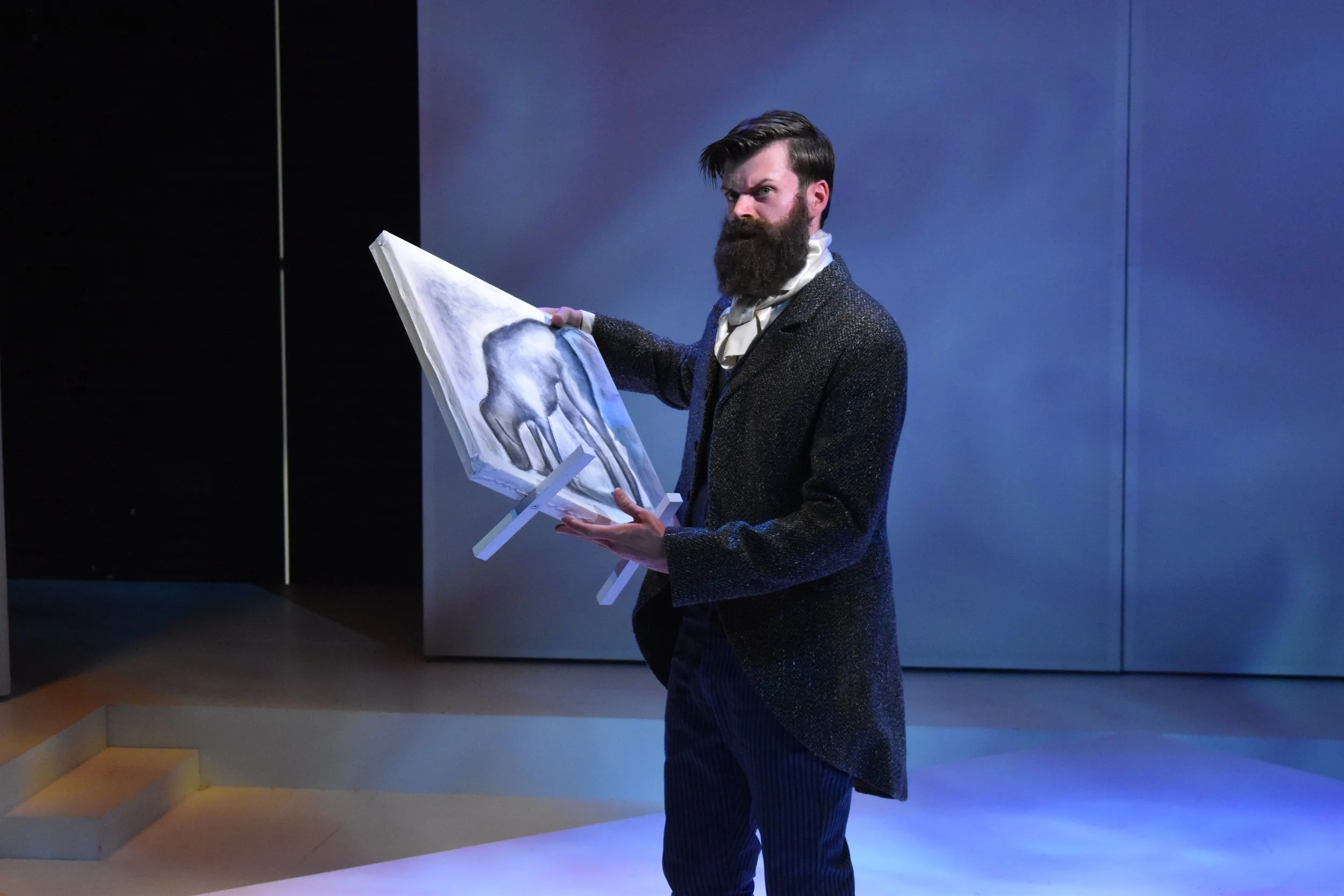 A man with a beard and a vintage-style suit holding an open art easel with a painting of an elephant, standing in a modern, dimly-lit room.