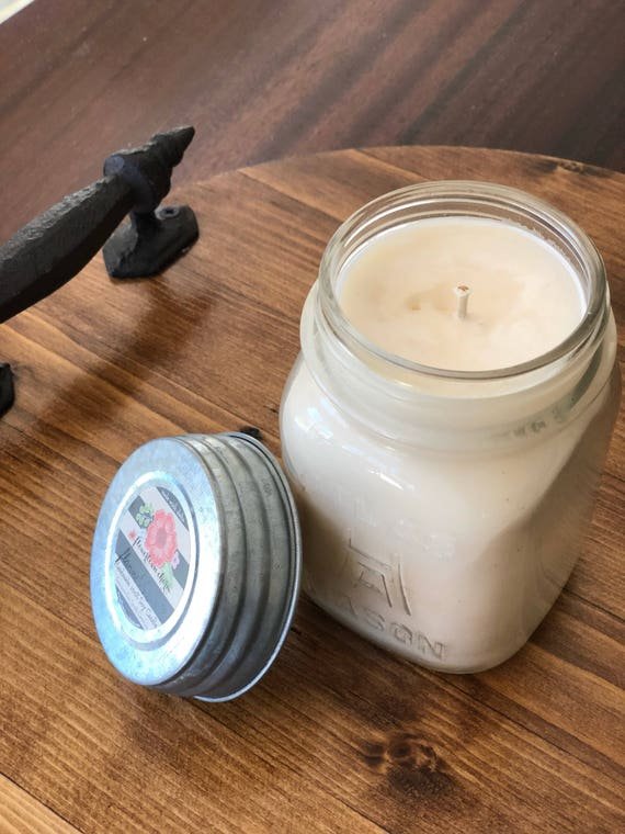 A holiday-themed table display with candles, decorative tags, a white towel with black text, and a glass jar filled with wooden spoons with holiday messages, set on a wooden table in a kitchen.