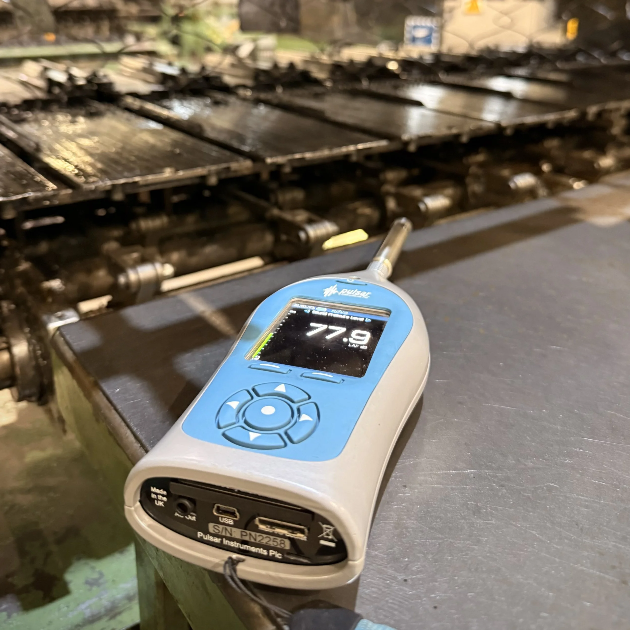 Noise meter on a metal table in a cotton mill noise assessment with the machinery behind it