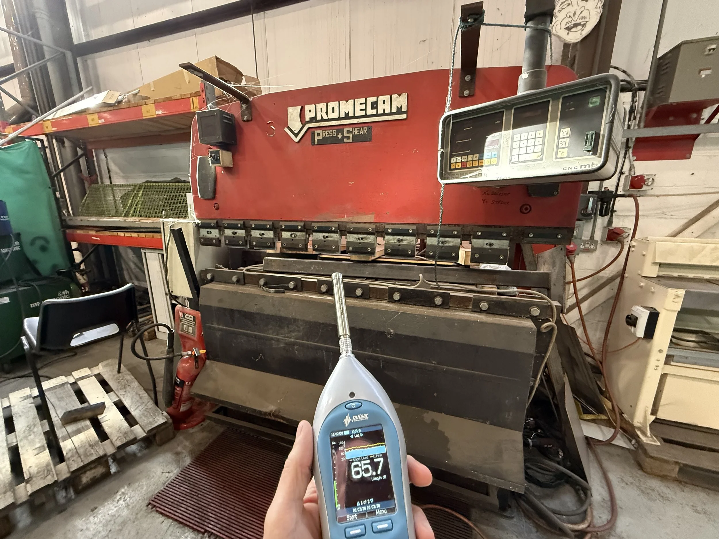 A large press, with a noise meter held in the hand in front of it for a noise assessment