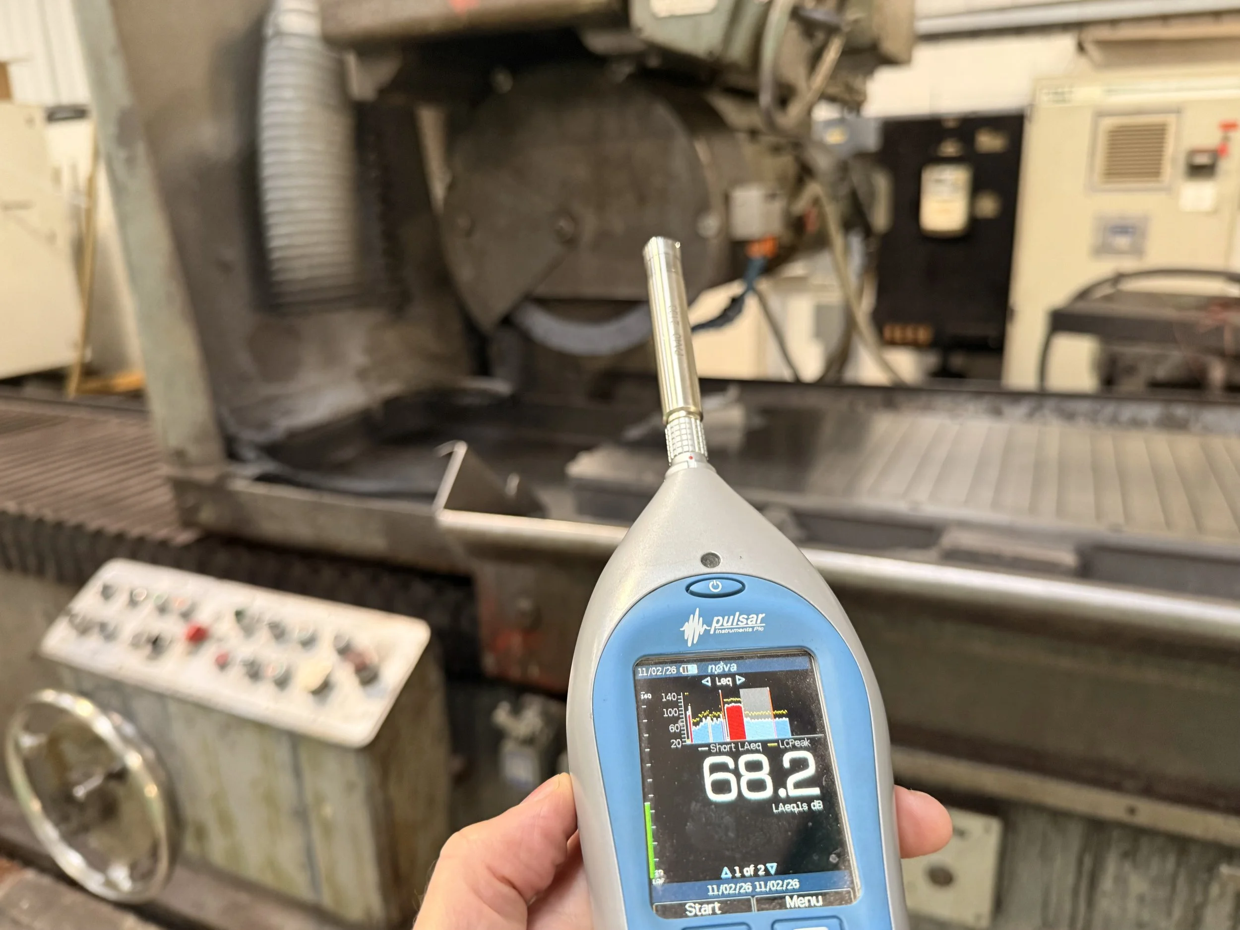 Noise meter being held next to a large old open CNC on a noise assessment.