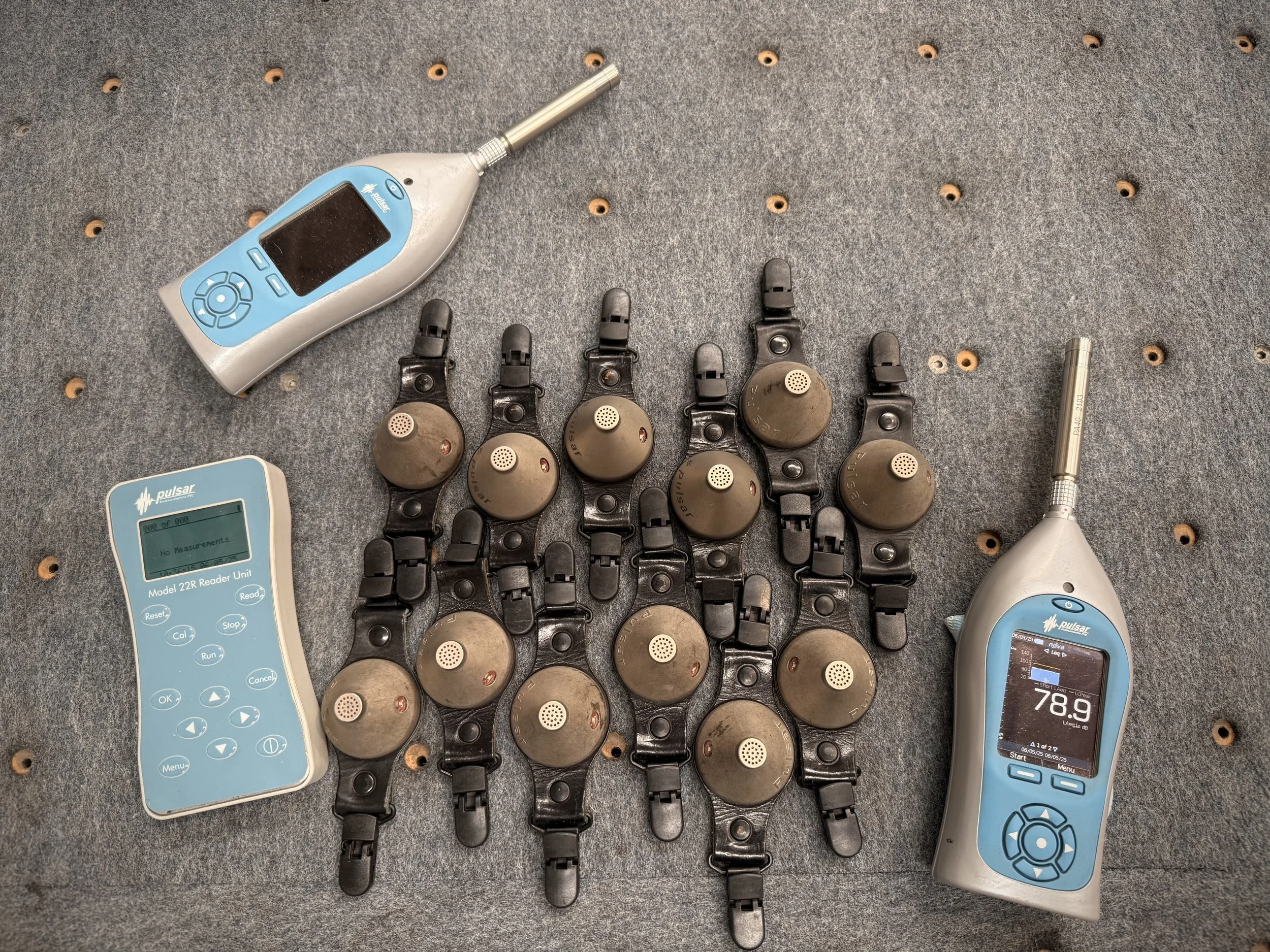 Noise meters and 12 noise dosimeters on a table during a noise assessment in a glass factory