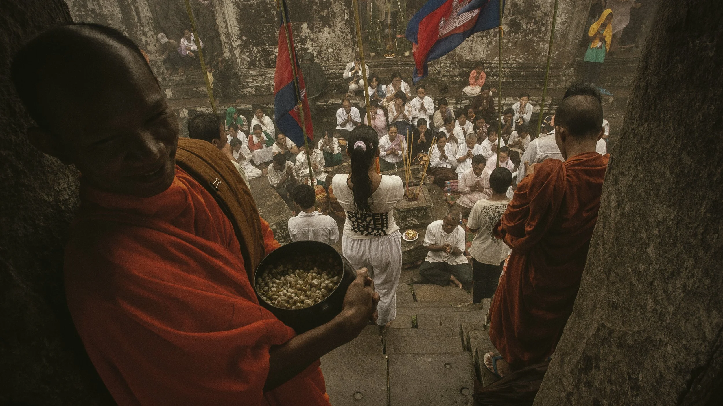 Within the temple complex, monks oversee the prayer ceremony as Cambodian worshippers join in a collective chant.