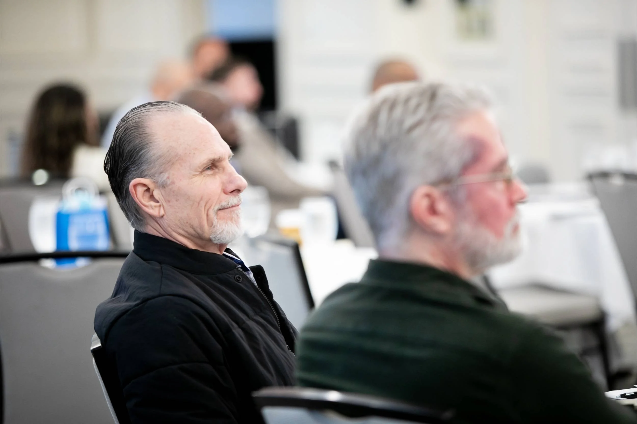 Several people seated in a conference room, attentively listening to a presentation.