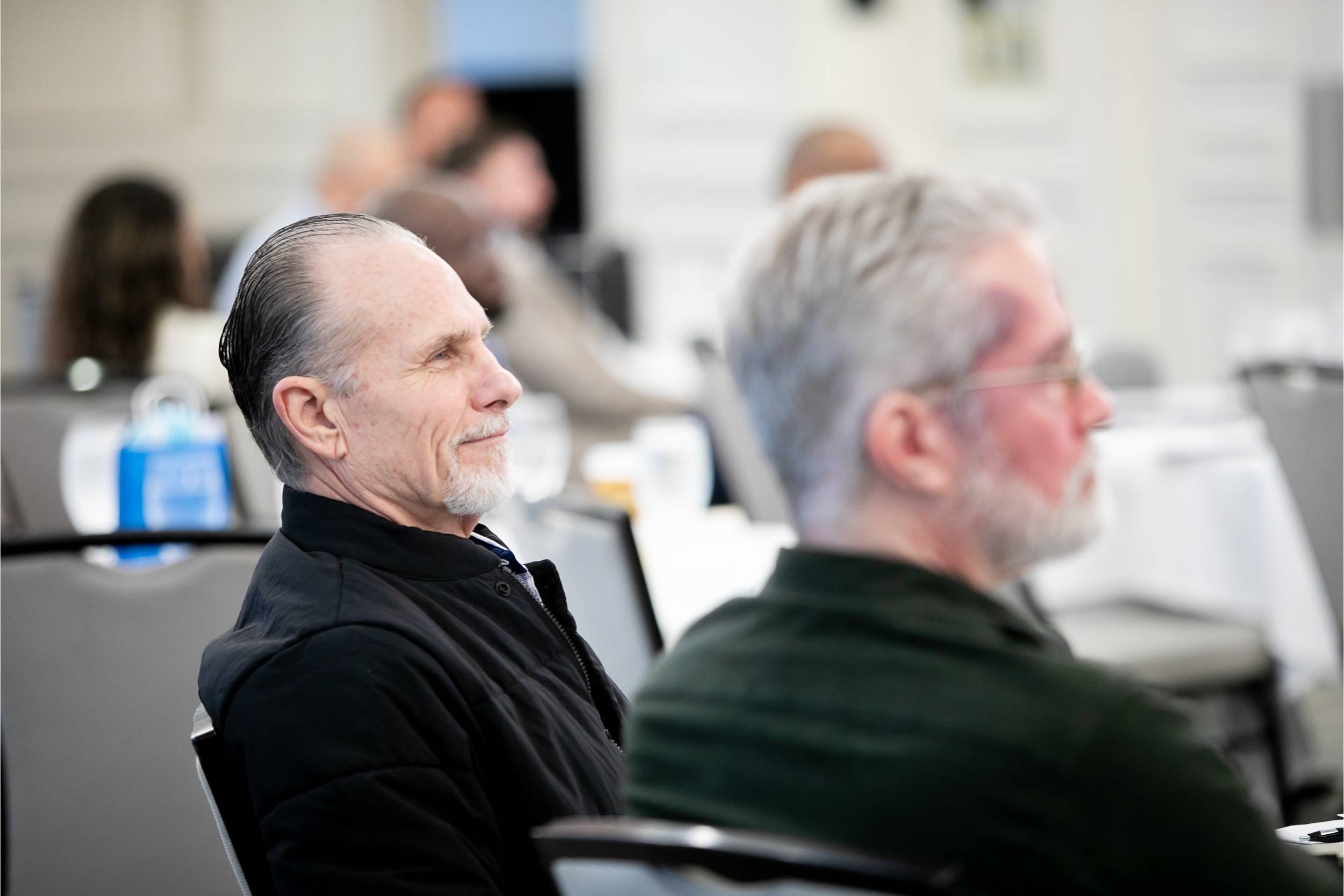 Several people seated in a conference room, attentively listening to a presentation.