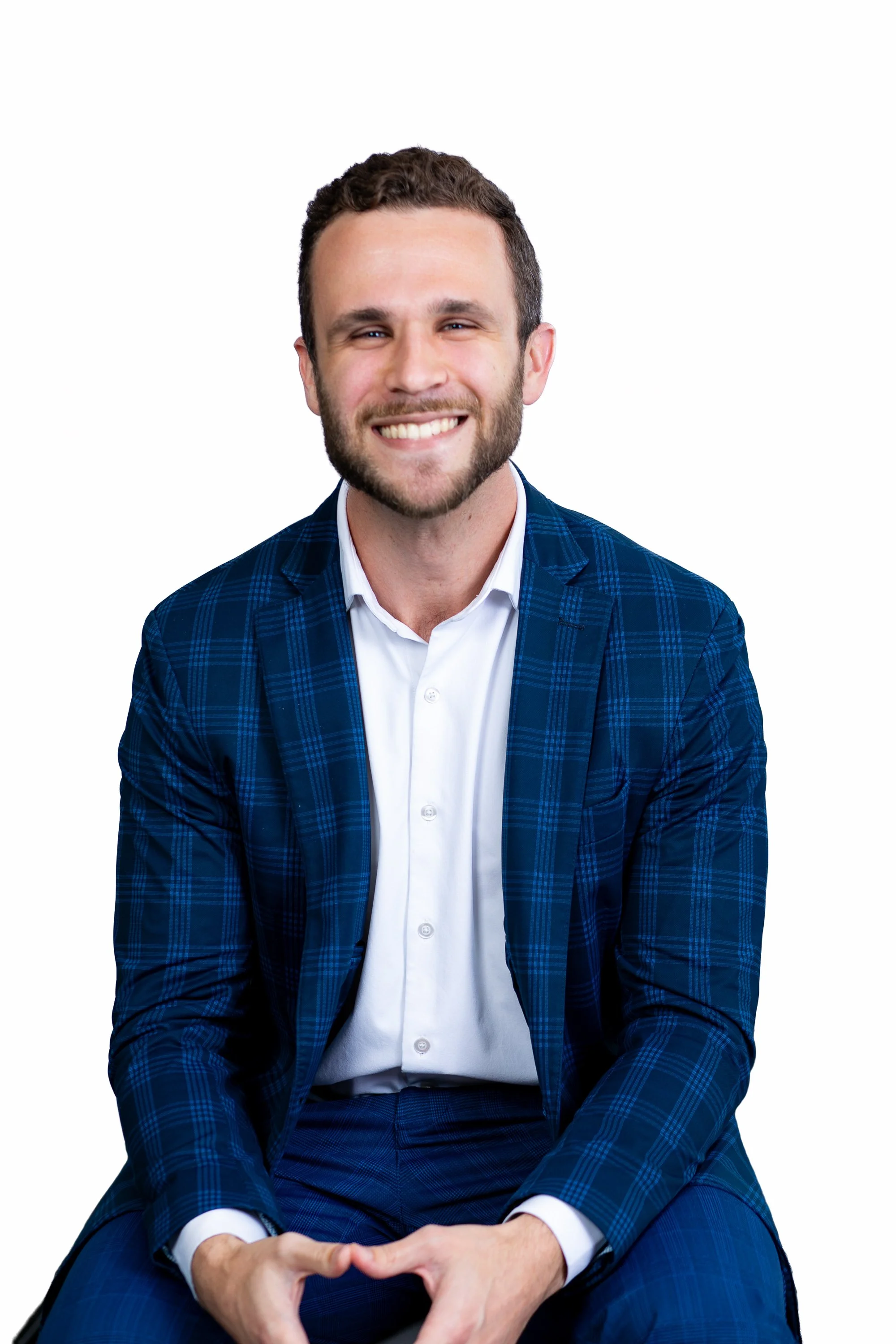A smiling man wearing a blue plaid suit and white shirt, sitting with hands forming a heart shape against a plain white background for a headshot with Cannonfire Photography.