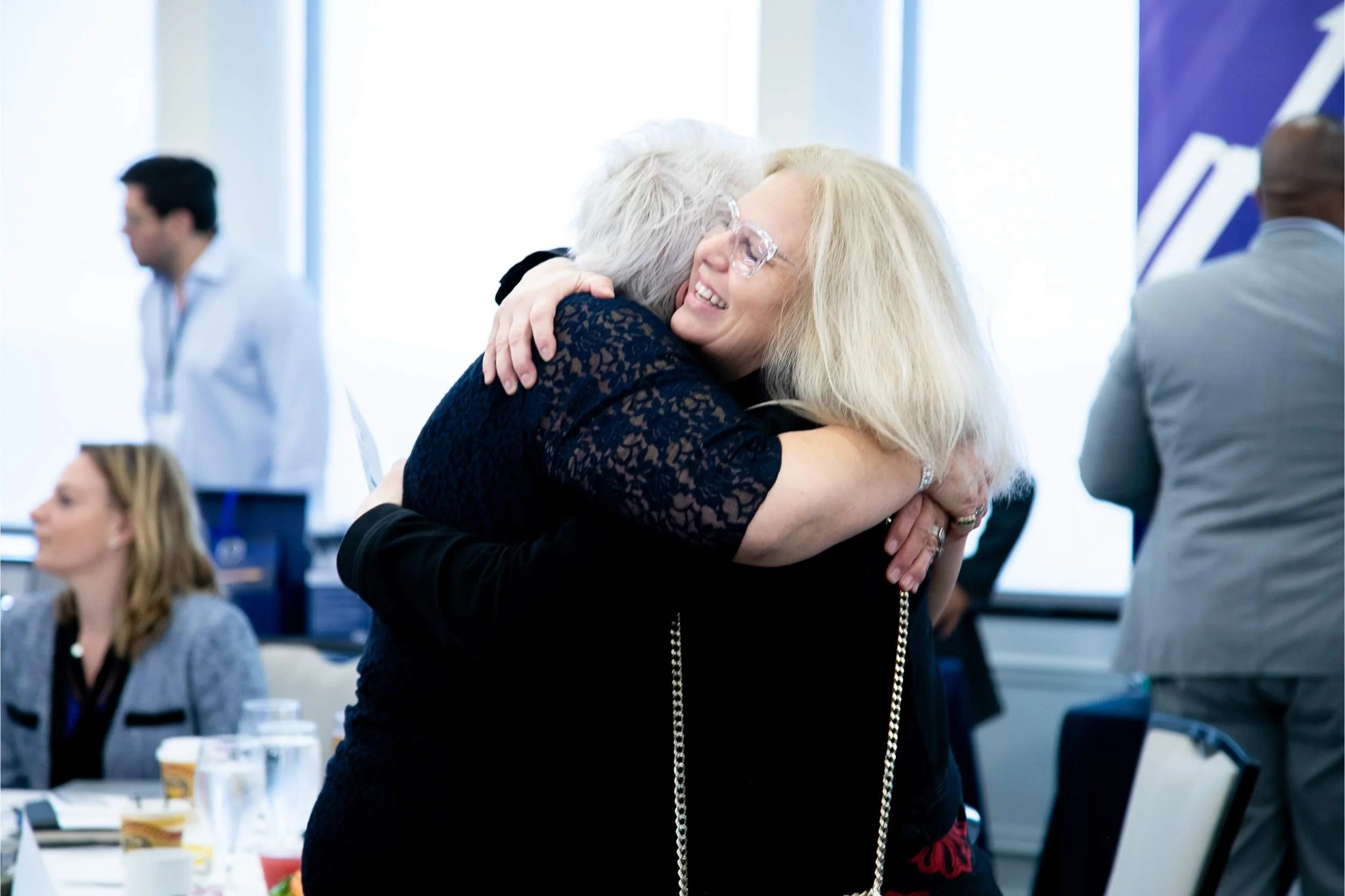 Two corporate event attendees hug one another during a networking session